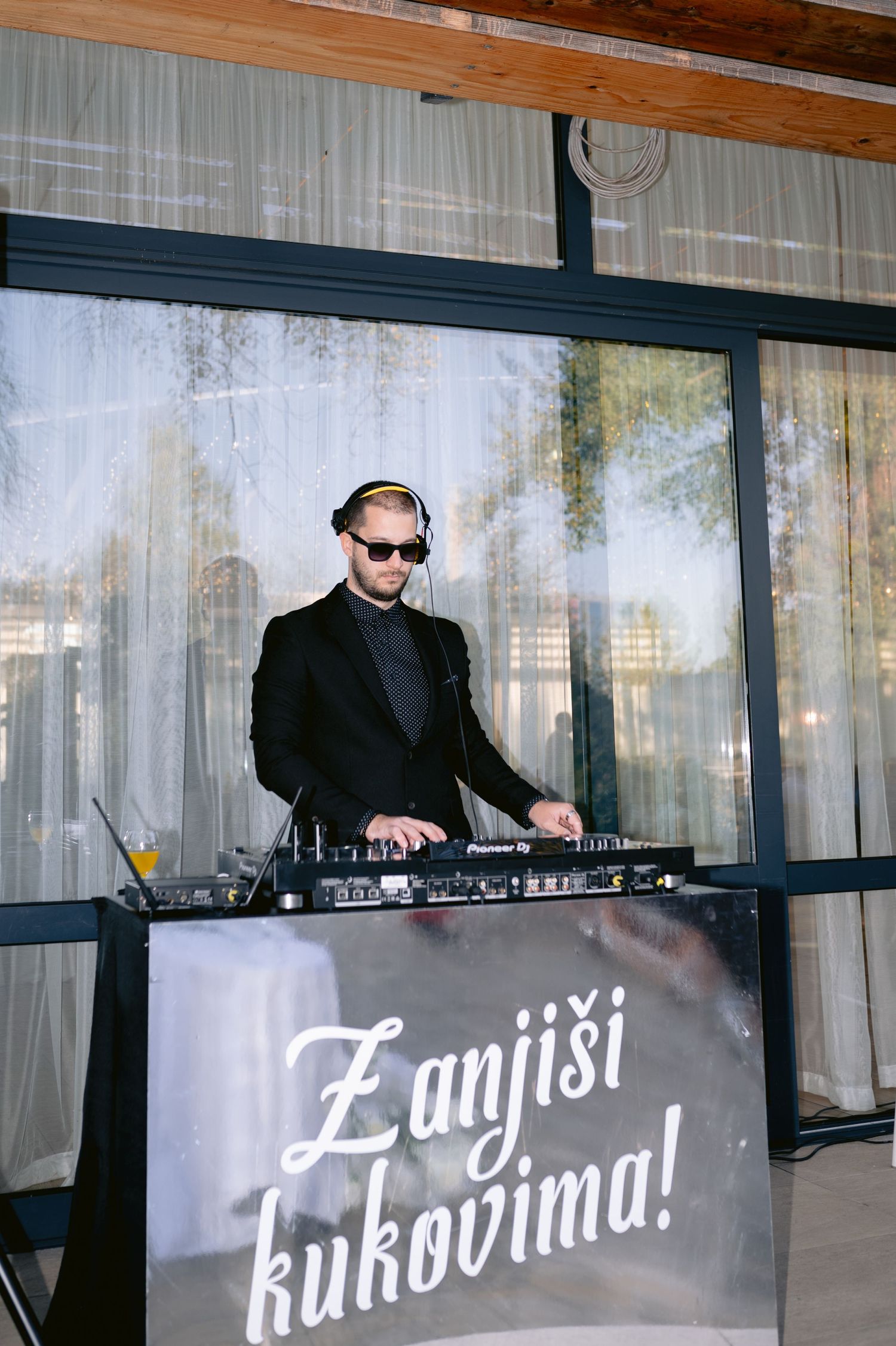 A DJ performs at a modern venue with white curtains and text signage in Finnish language displayed.
