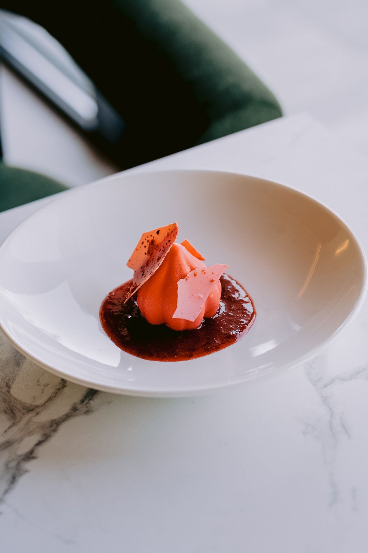 Elegant plated dessert with pink mousse, berry coulis, and chocolate shards in a white bowl on marble.