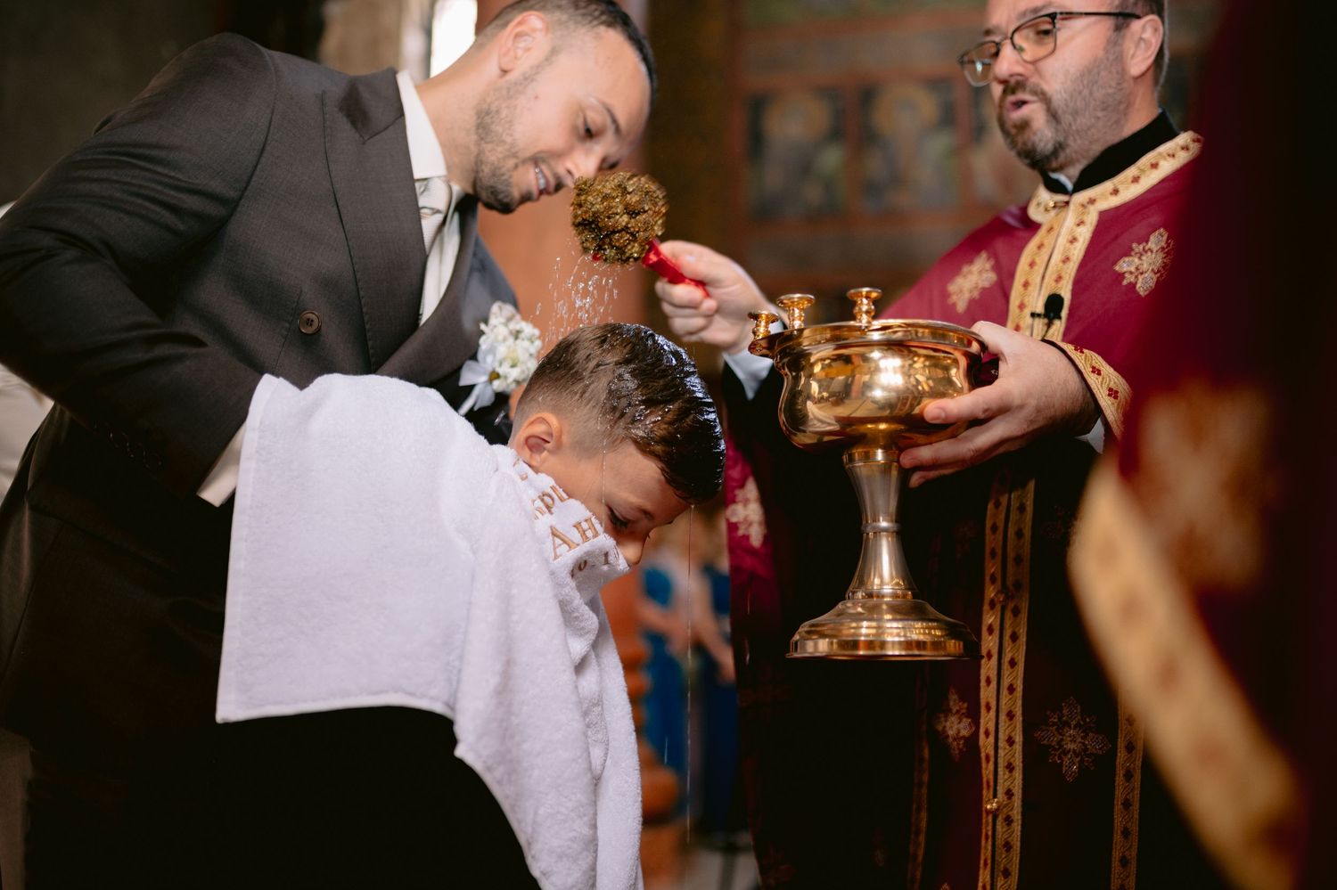 Orthodox priest performing a baptism ceremony, pouring holy water on a child's head from a golden chalice.