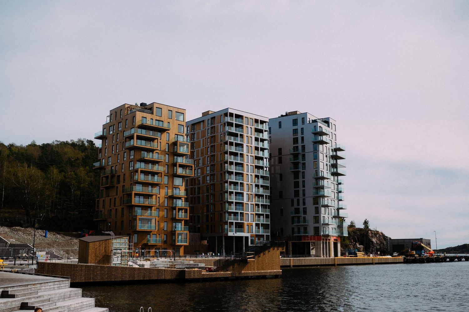 Modern waterfront apartment buildings with glass balconies reflect in calm waters at sunset.
