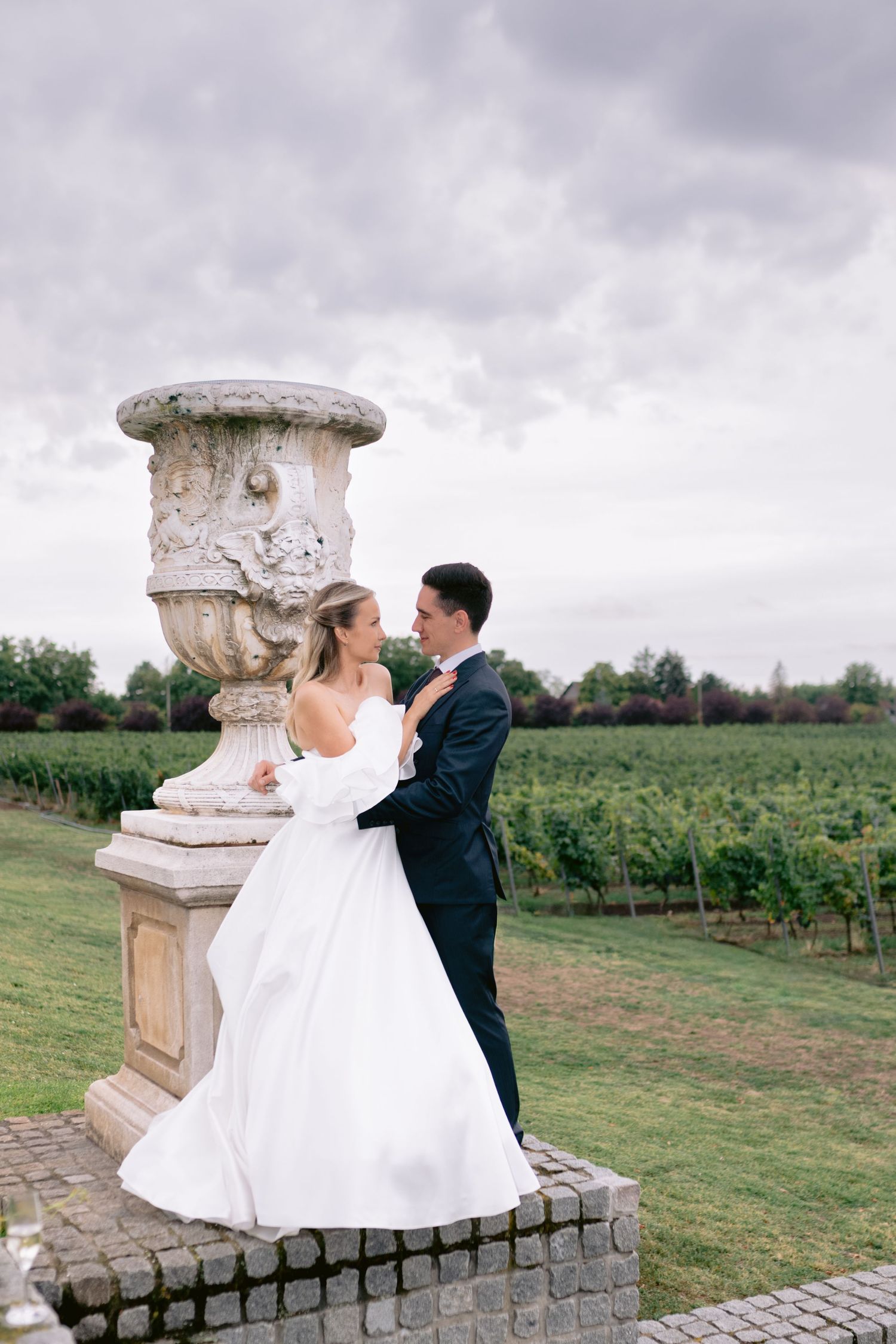 Romantični svadbeni portret pored dekorativne kamene vaze sa pejzažom vinograda u pozadini vinarija Zvonko Bogdan.
