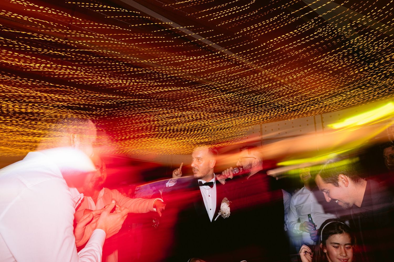 People dancing at a nightclub under red and yellow lighting with a string light ceiling decoration.