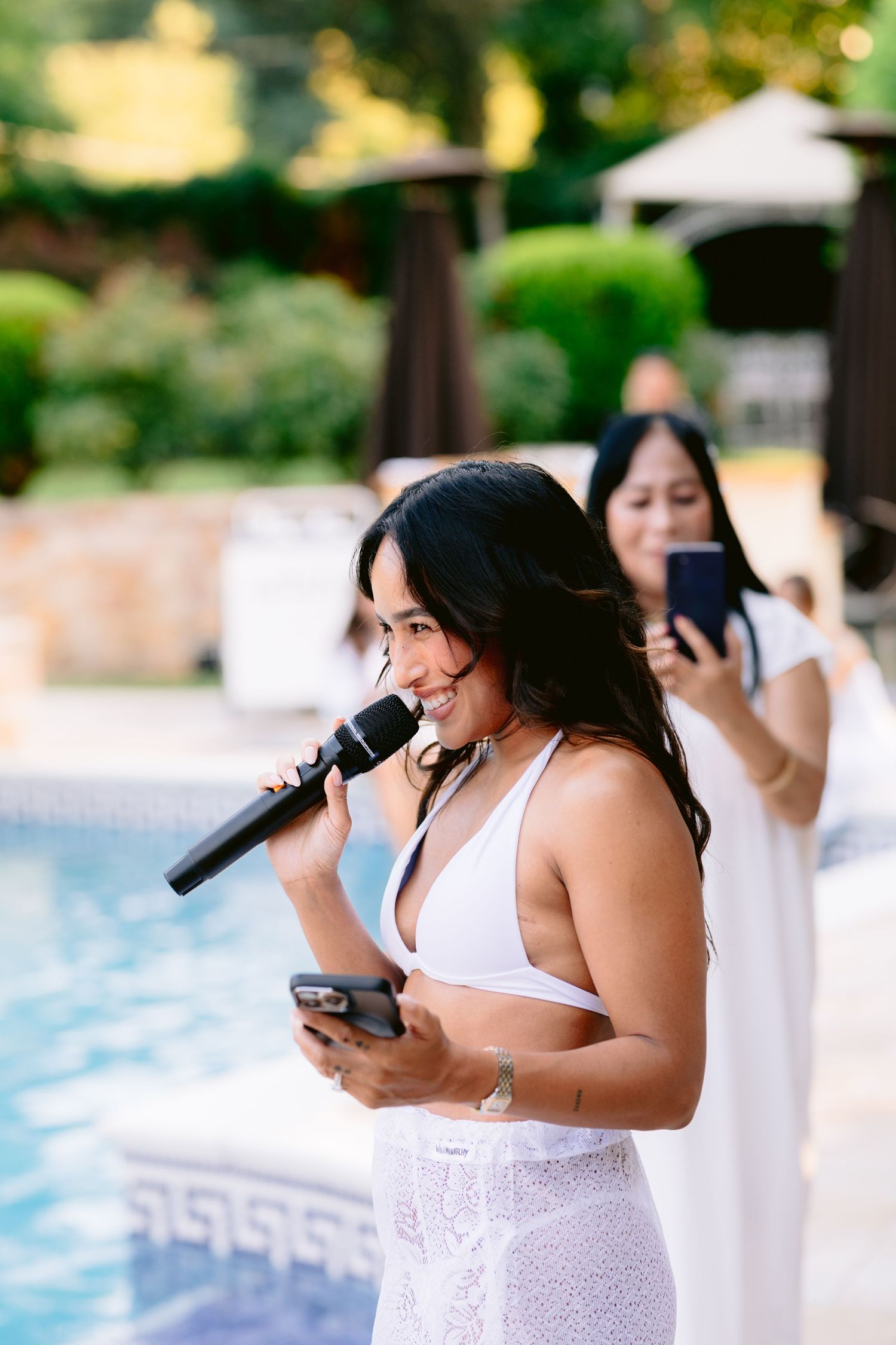 Gošća u bijelom bikiniju drži govor na mikrofonu pored bazena, pool party vjenčanje Villa Slatina Banja Luka