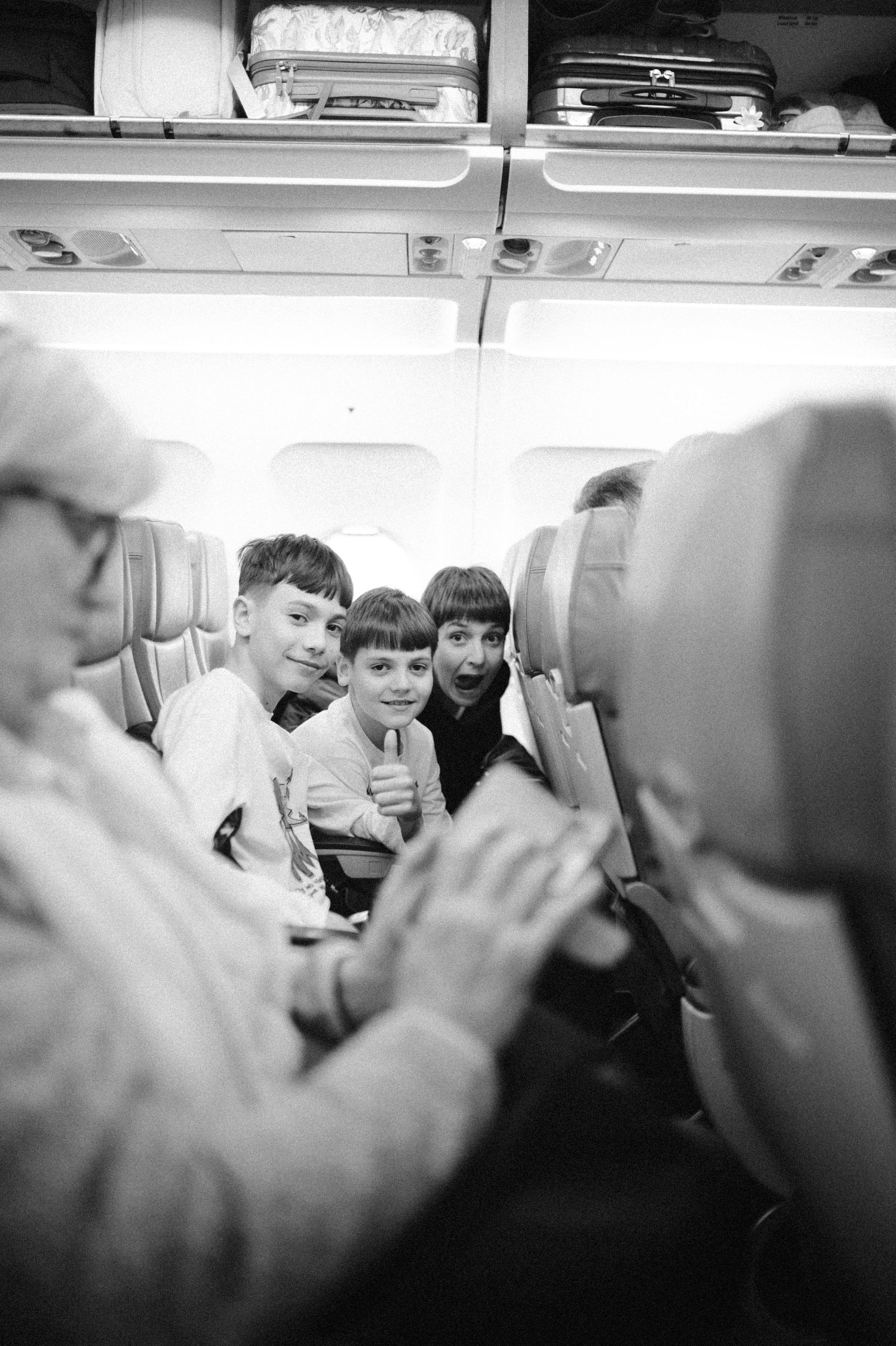 A black and white photograph taken inside an airplane cabin showing passengers seated together in vintage style.