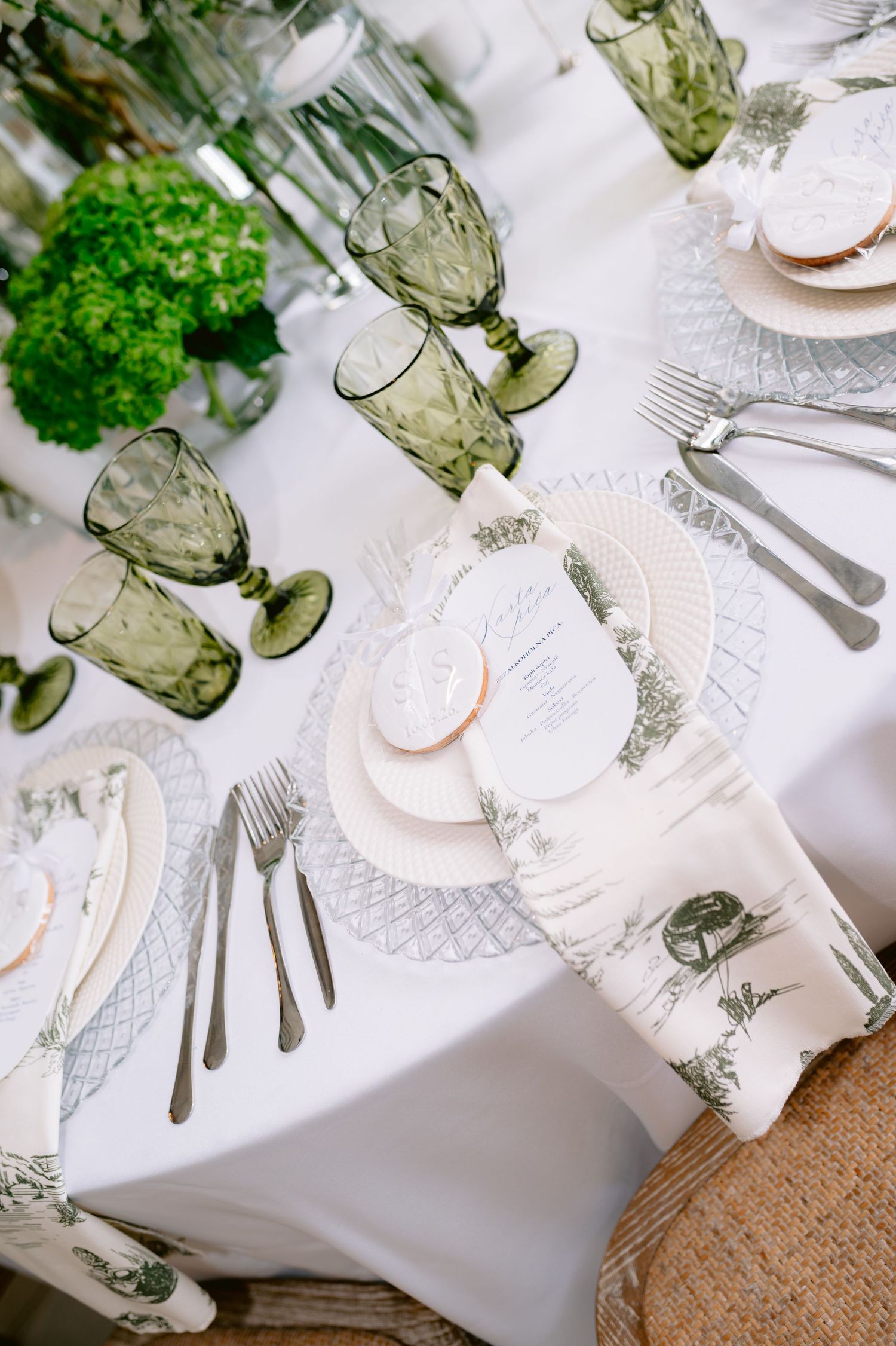 Elegant wedding table setting with green goblets, white linens, floral napkins, and fresh hydrangea centerpieces.
