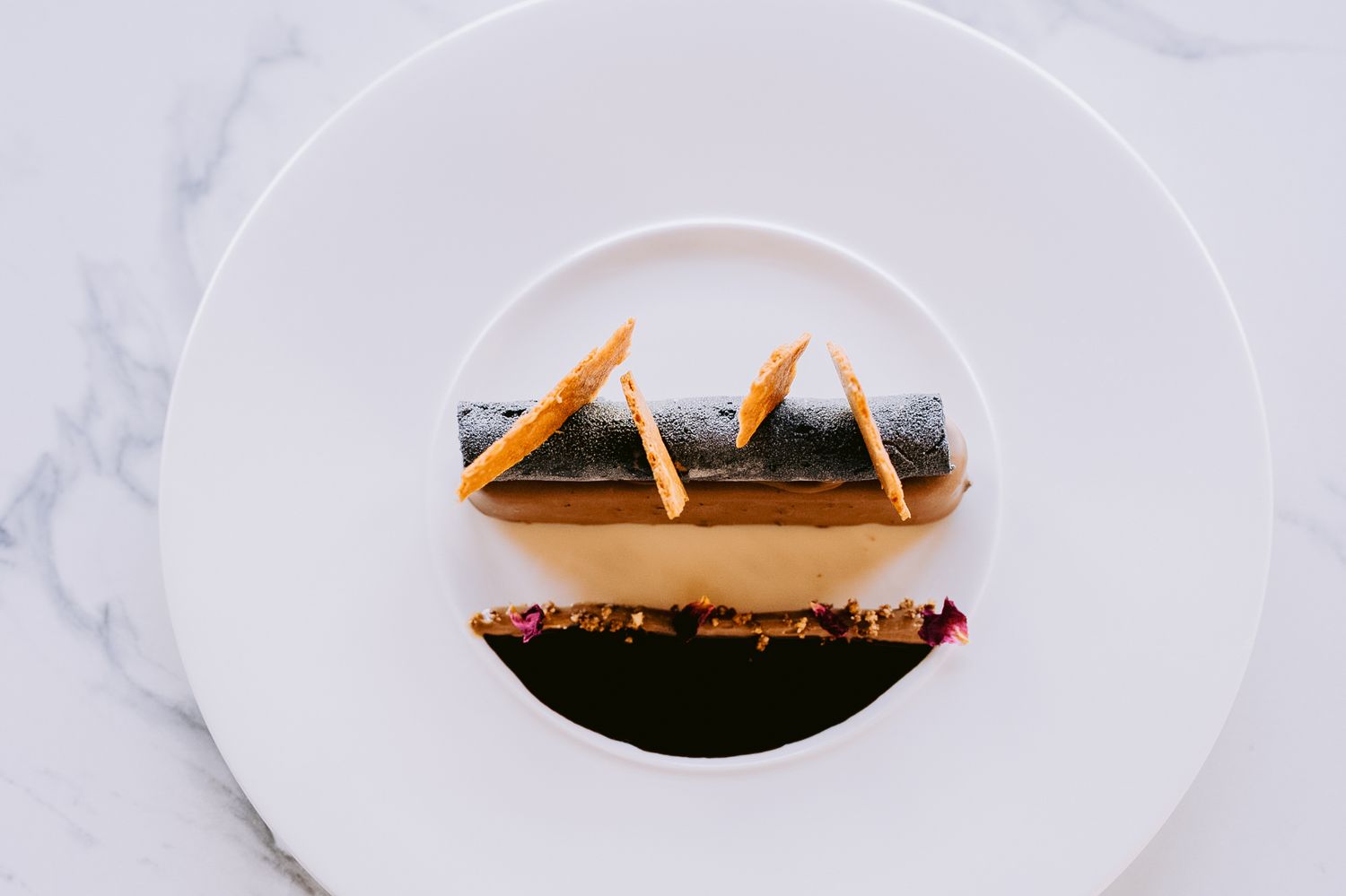 Minimalist plated dessert on white marble surface with geometric presentation.