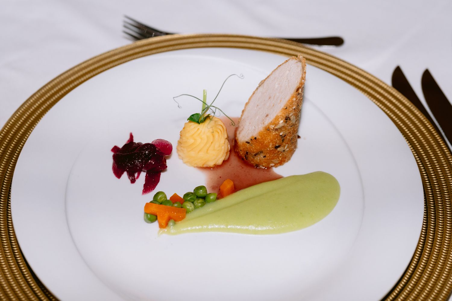 Gourmet plated dish with colorful sauces and garnishes on gold-rimmed white plate.