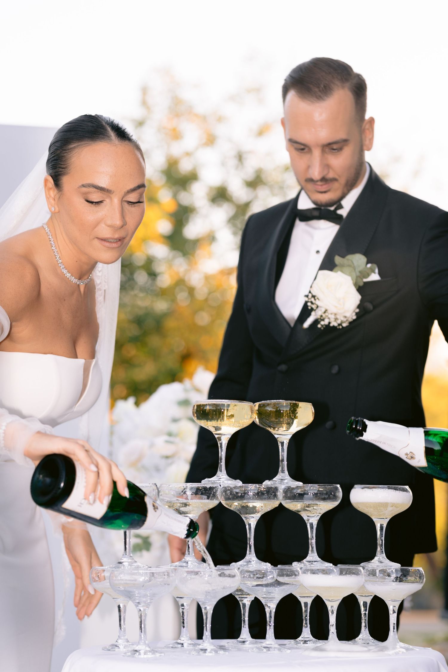 A champagne tower being carefully poured at an elegant wedding reception with crystal glasses arranged in layers.