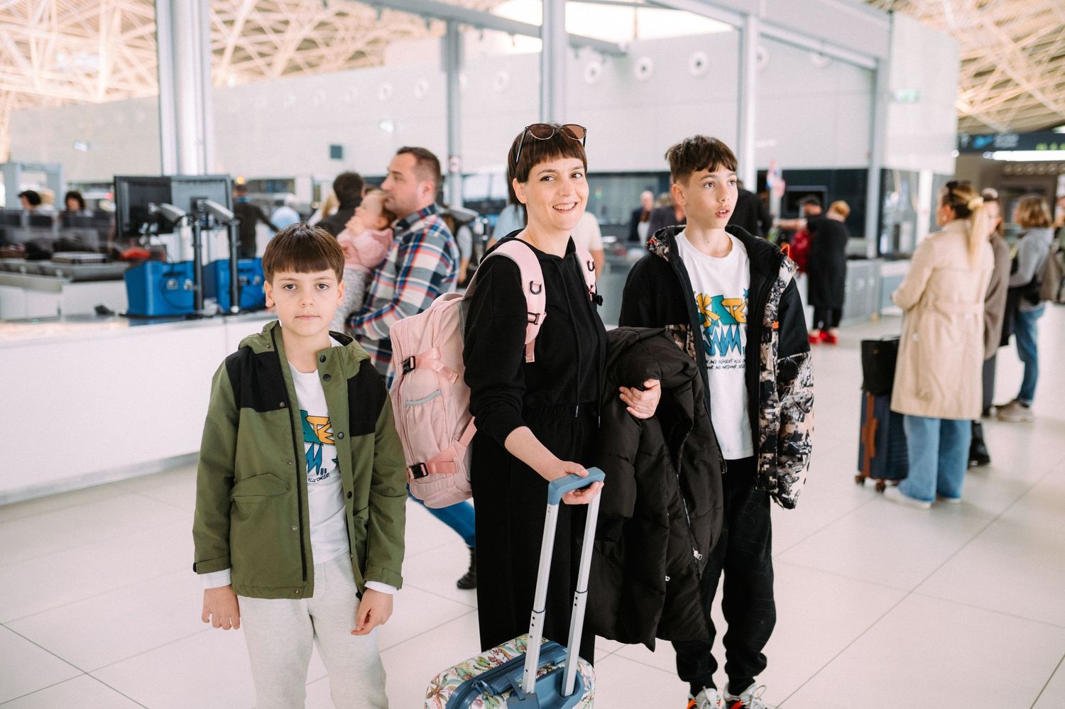 A group of travelers walking through an airport terminal with luggage and carry-on bags.