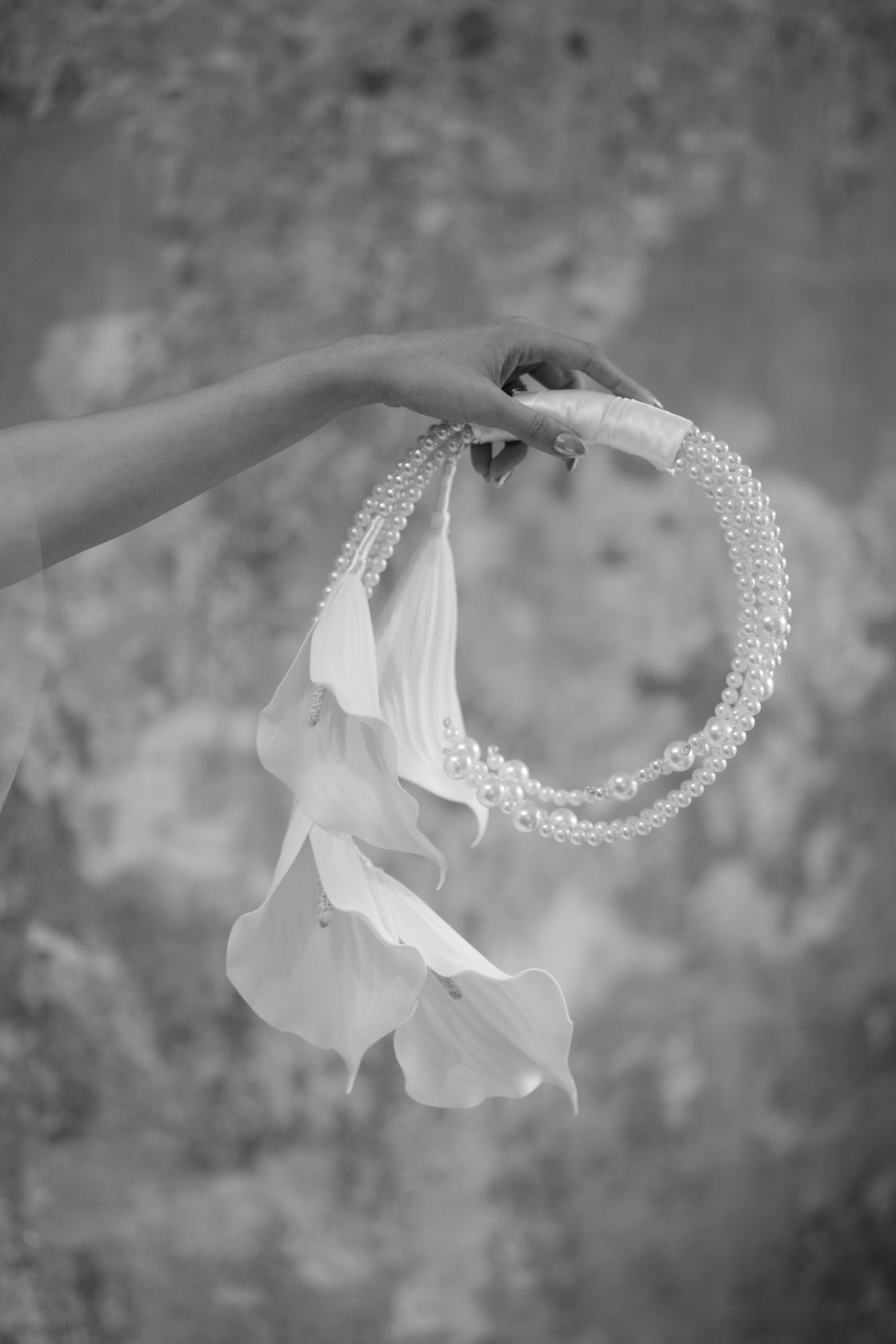 Hand holds delicate pearl crown with flowing white ribbons in black and white photograph.