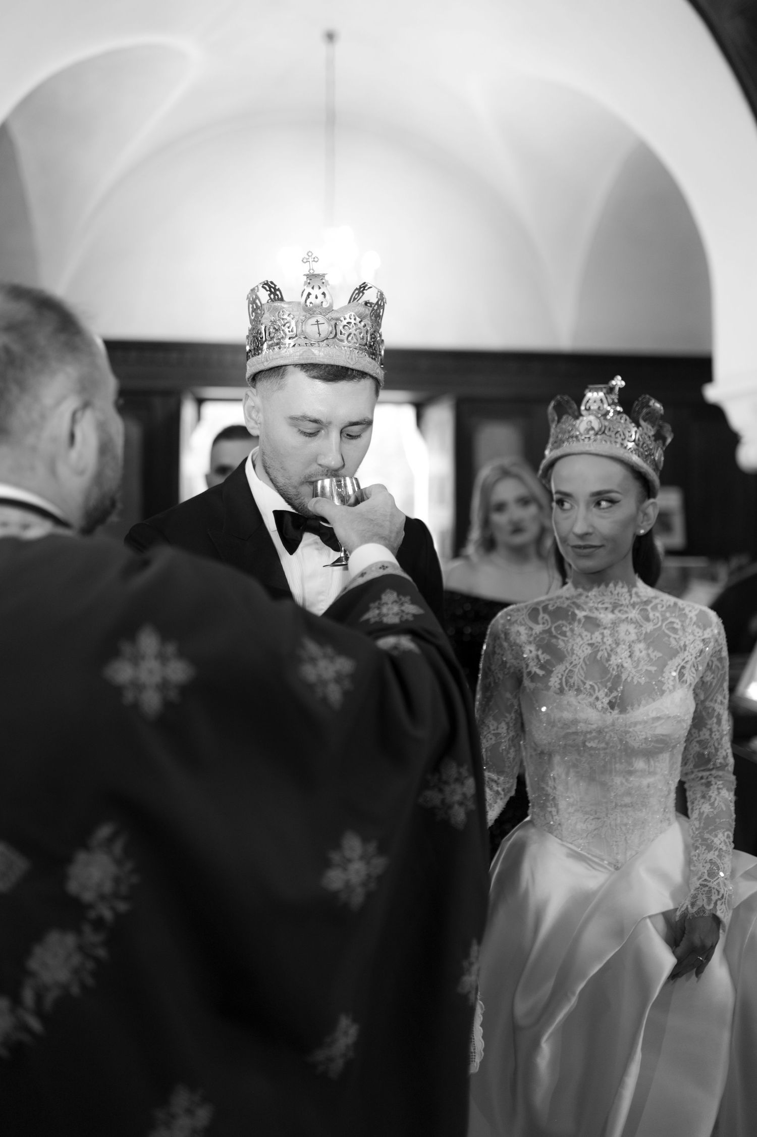 A black and white photograph of a wedding ceremony with the couple wearing crowns and formal attire.