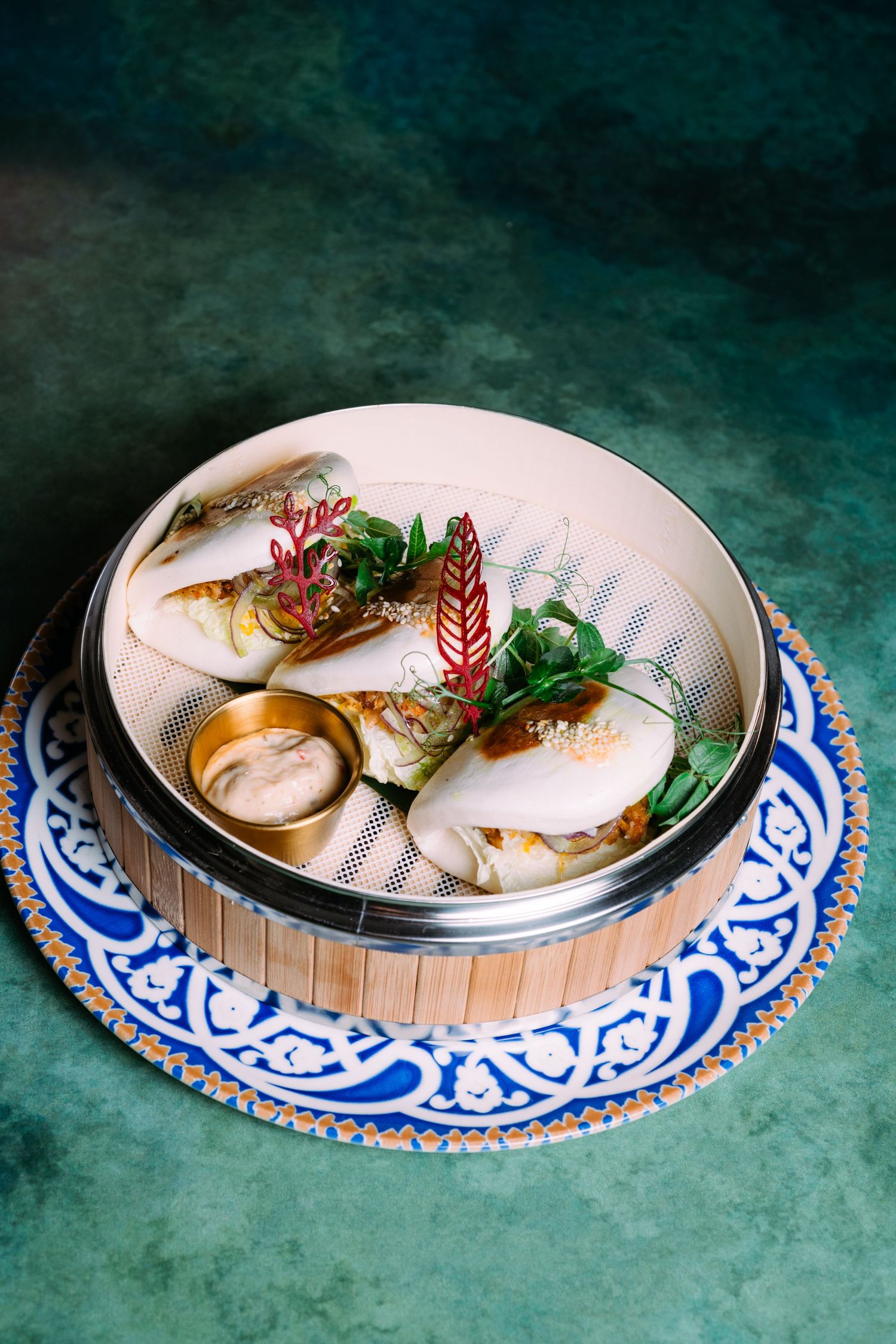 Asian steamed dumplings served in bamboo basket on blue and white porcelain plate against teal background.