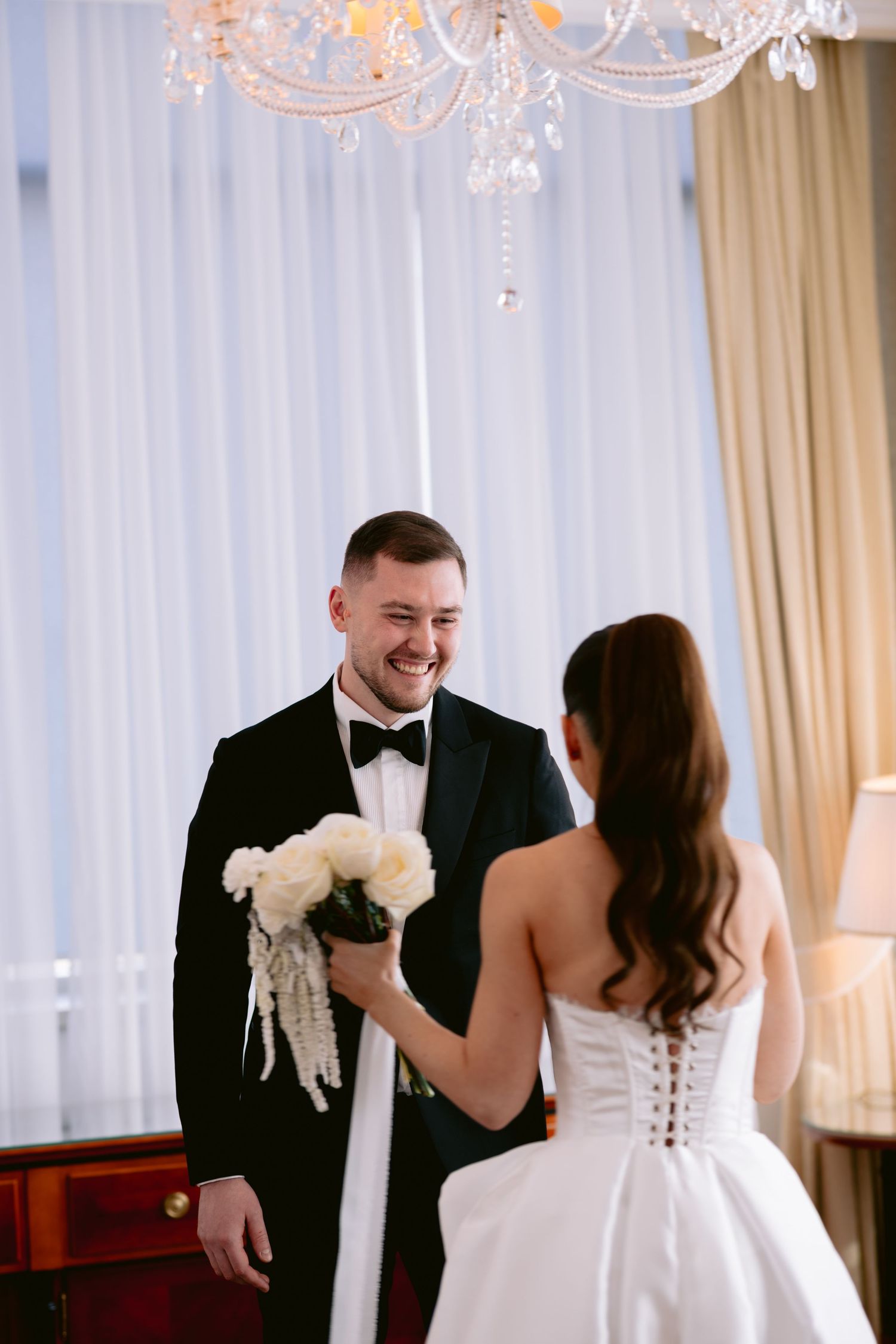 A couple shares a joyful first dance moment at their wedding reception in an elegant room with white drapes.