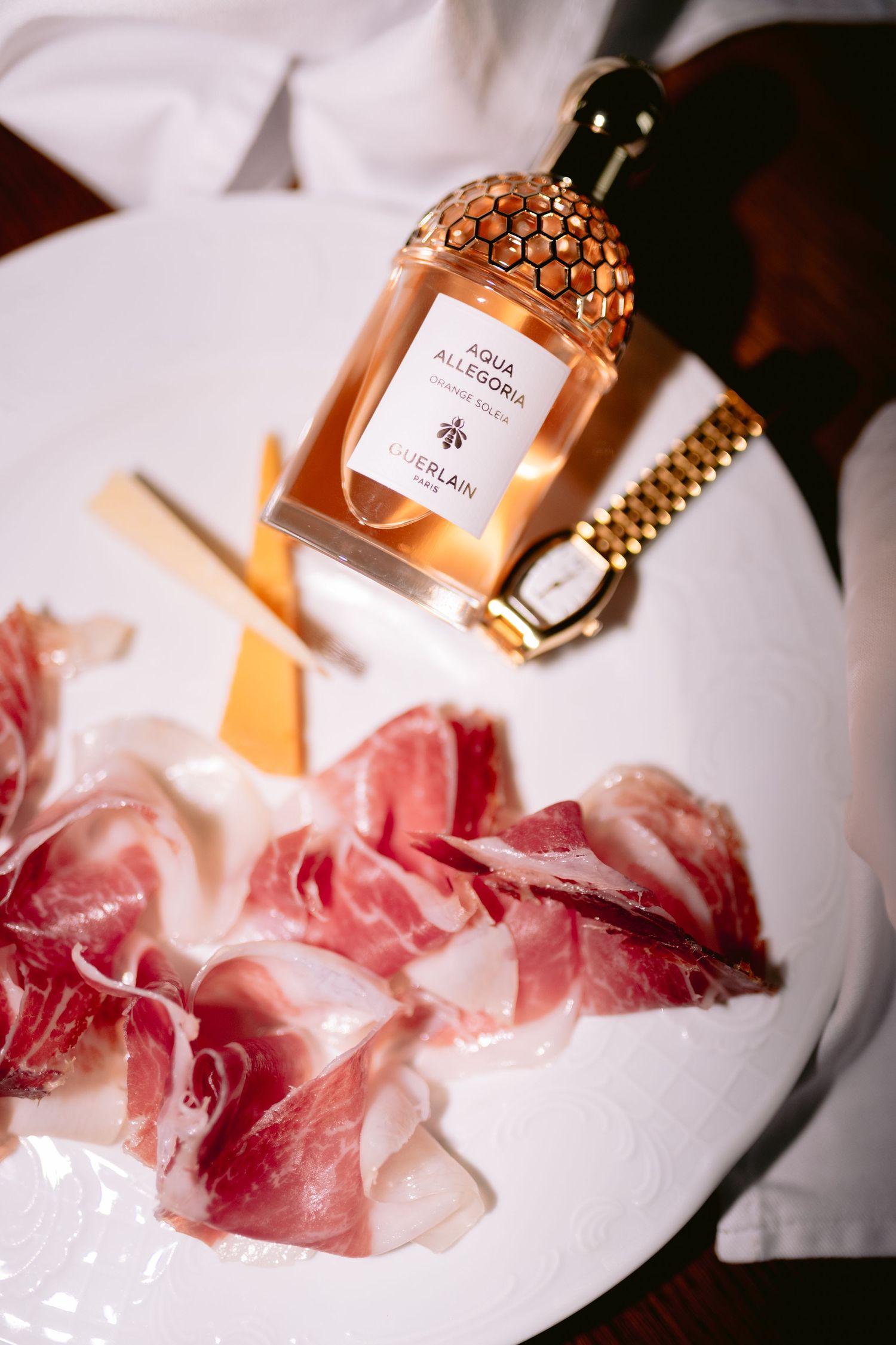 Perfume bottle arranged with delicate pink rose petals on white surface.