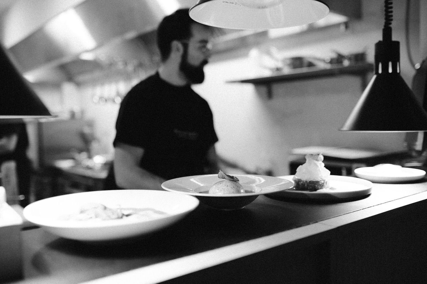 Black and white image of plated dishes being prepared in a restaurant kitchen.