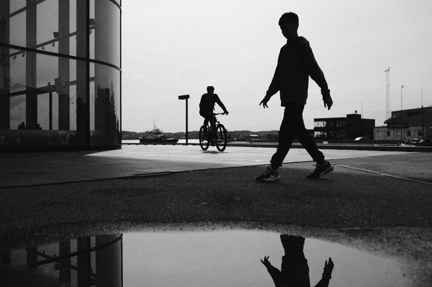 A silhouetted figure walks past a modern architectural building with geometric lines and shadows.