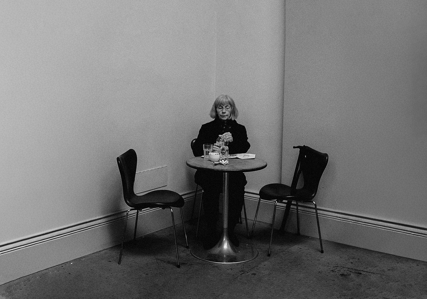 Black and white panoramic image shows a series of empty chairs against white walls in a minimalist interior space.