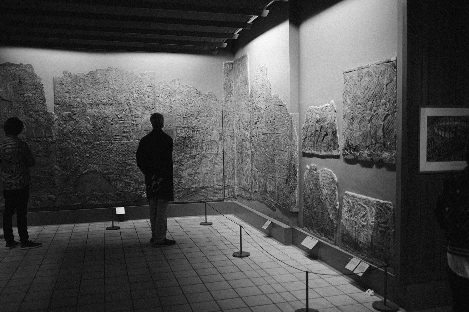 Art gallery visitors view detailed black and white drawings displayed on white walls in a museum exhibition space.