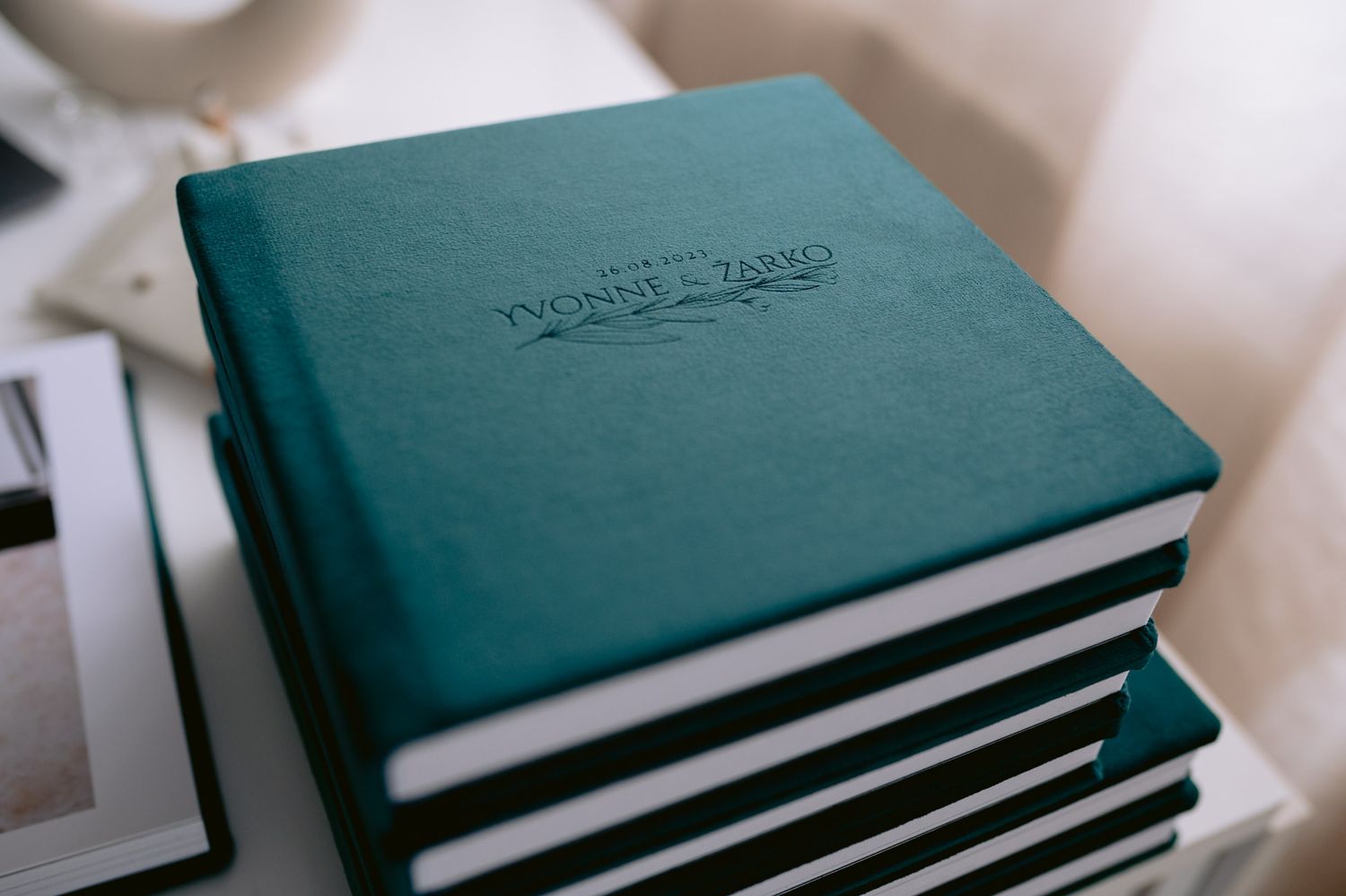 Stack of teal hardcover wedding photo albums with embossed names on a white surface.