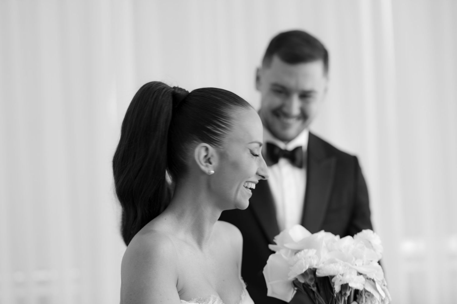 A black and white photo of a bride and groom sharing a joyful moment during their wedding ceremony.