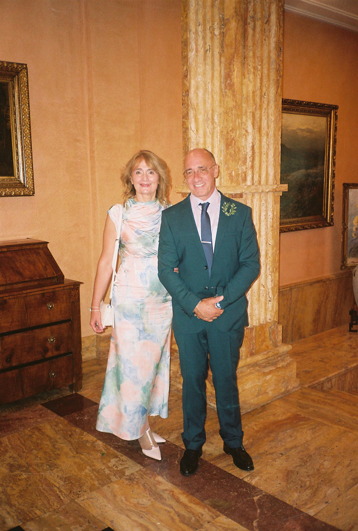 A couple poses together in an elegant indoor setting with marble floors and ornate decor.