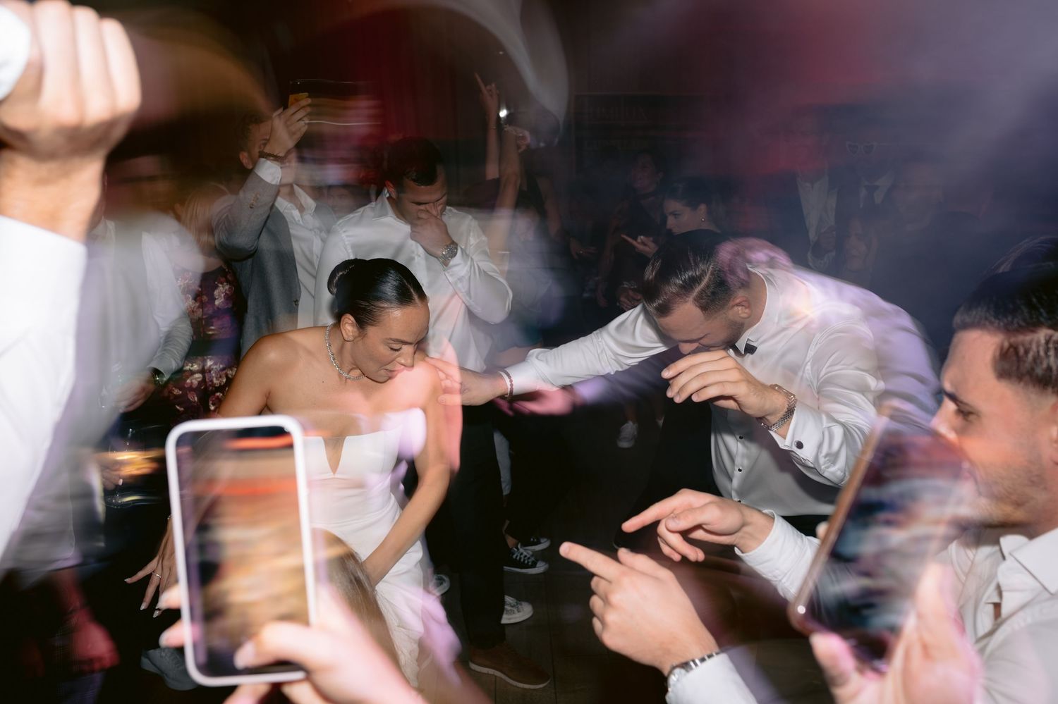 Wedding guests dance and celebrate together on the dance floor at an indoor reception venue.
