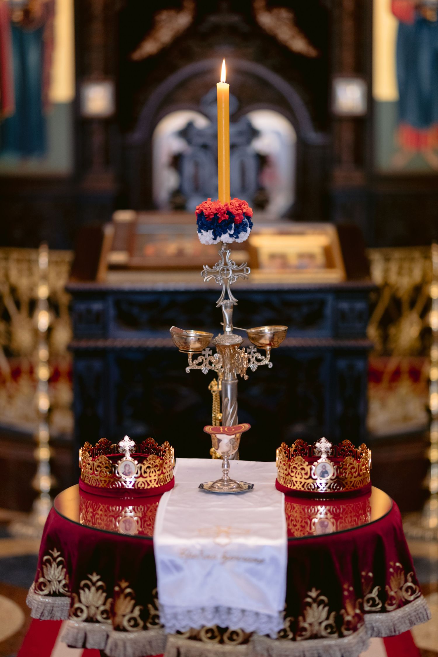 Ornate crowns and candles displayed on burgundy velvet cloth for a religious ceremony or royal celebration.