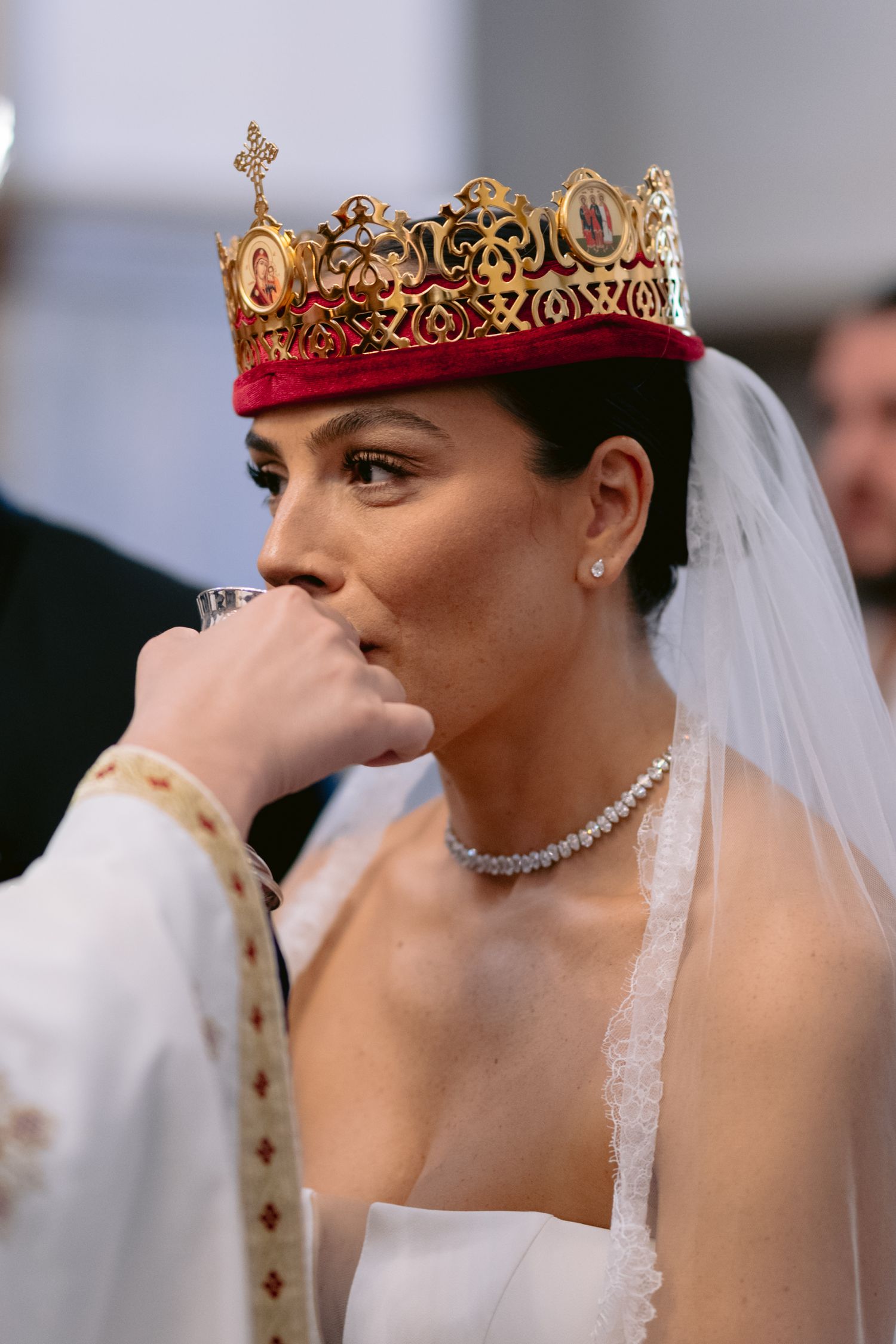 A bride wearing a delicate crown and veil wipes away tears during an emotional wedding ceremony moment.