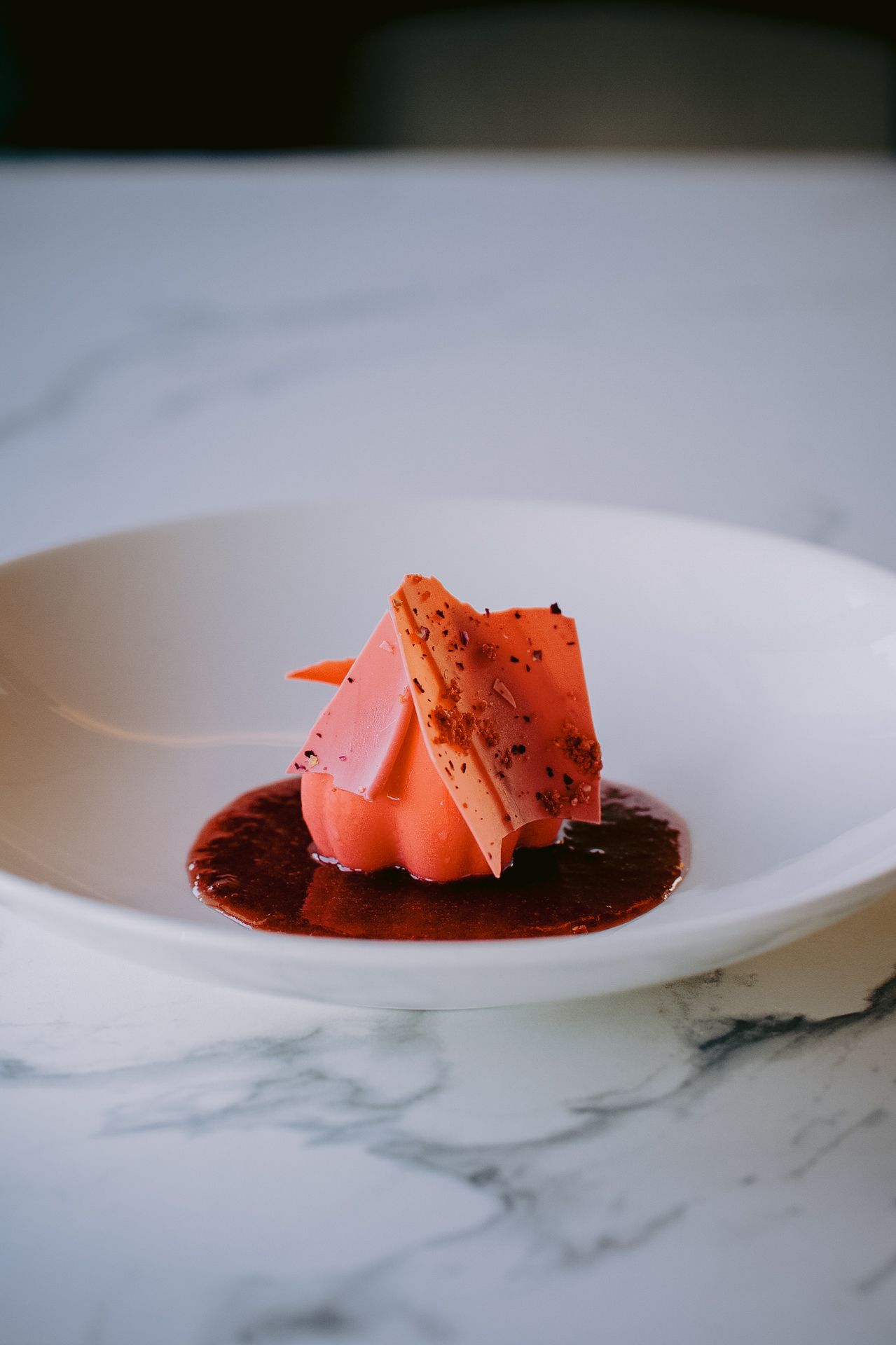 Pink-colored dessert pieces plated artistically on white marble surface.