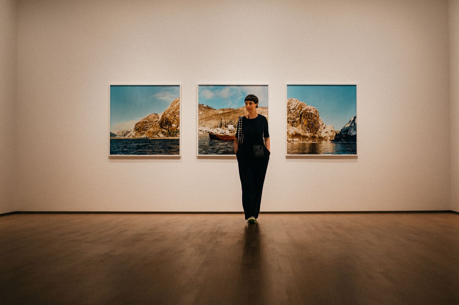 A series of landscape photographs displayed in a minimalist gallery space with white walls and wooden floors.