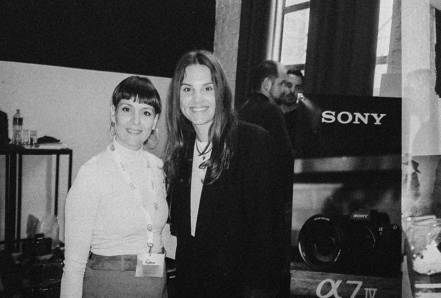 A black and white photo of two people posing together in front of a Sony display.
