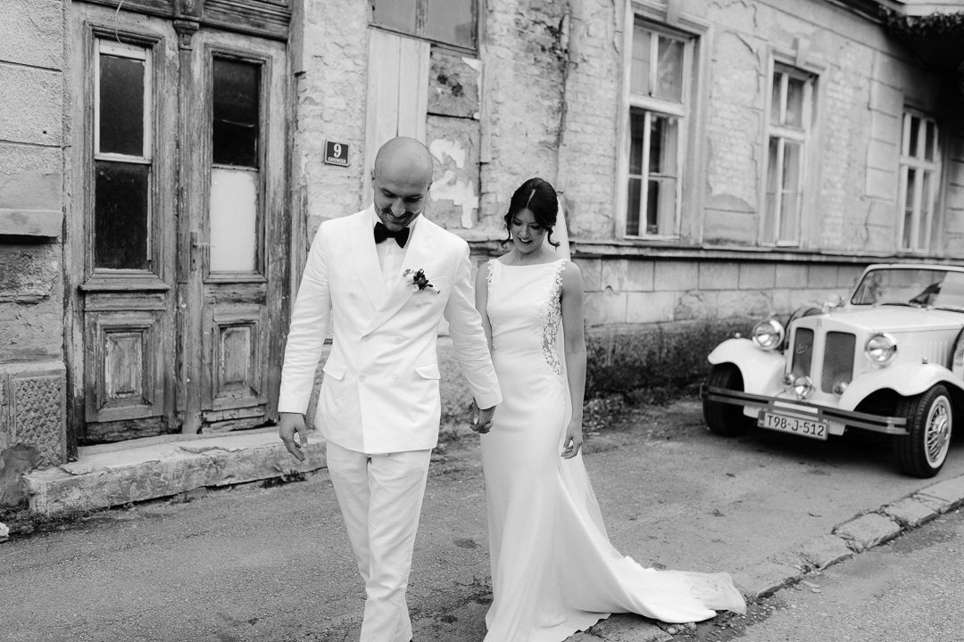 Black and white photo of couple walking down urban street in wedding attire.