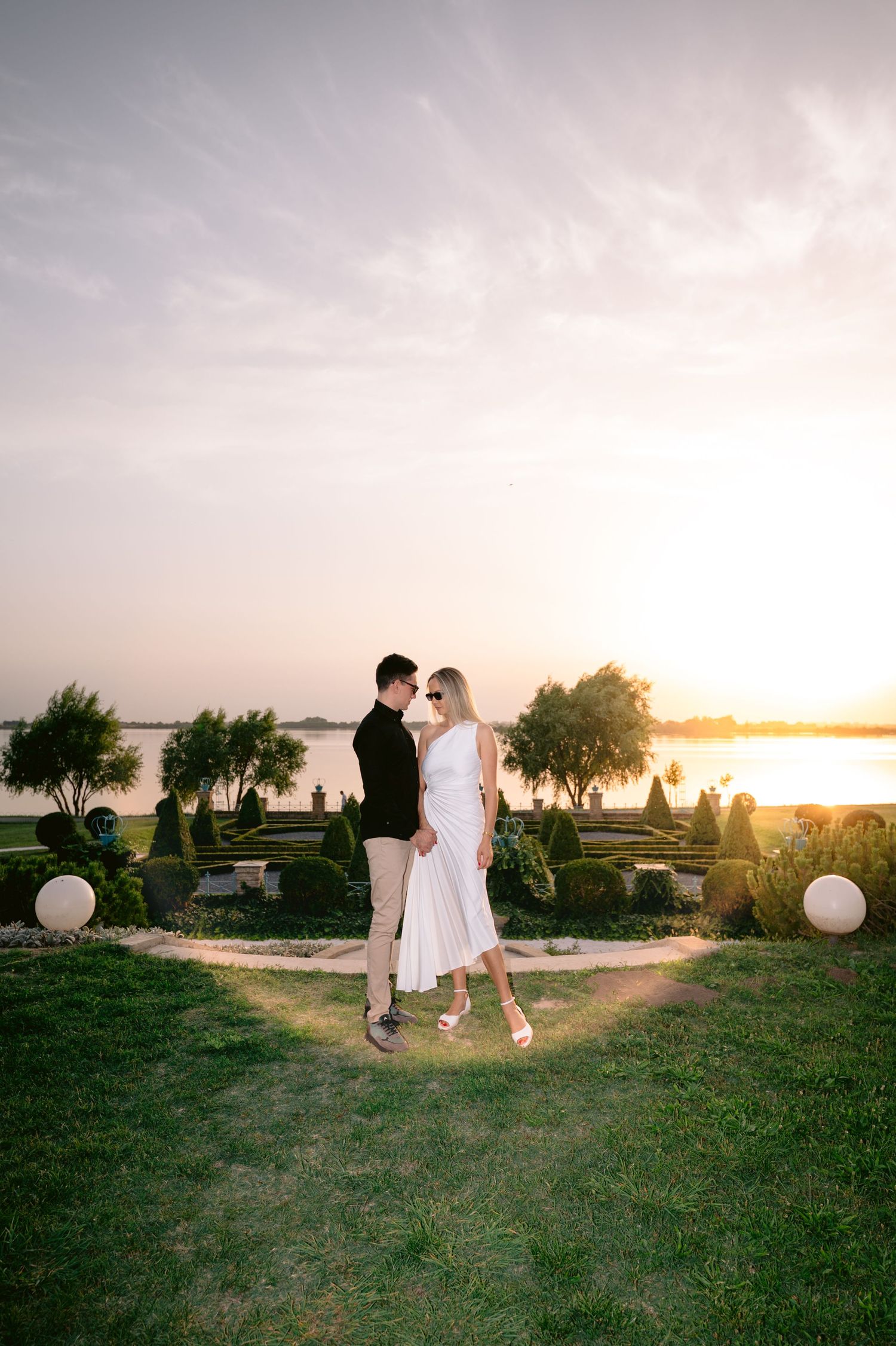 Romantic sunset photoshoot in a grassy field with white balloons and soft golden light.
