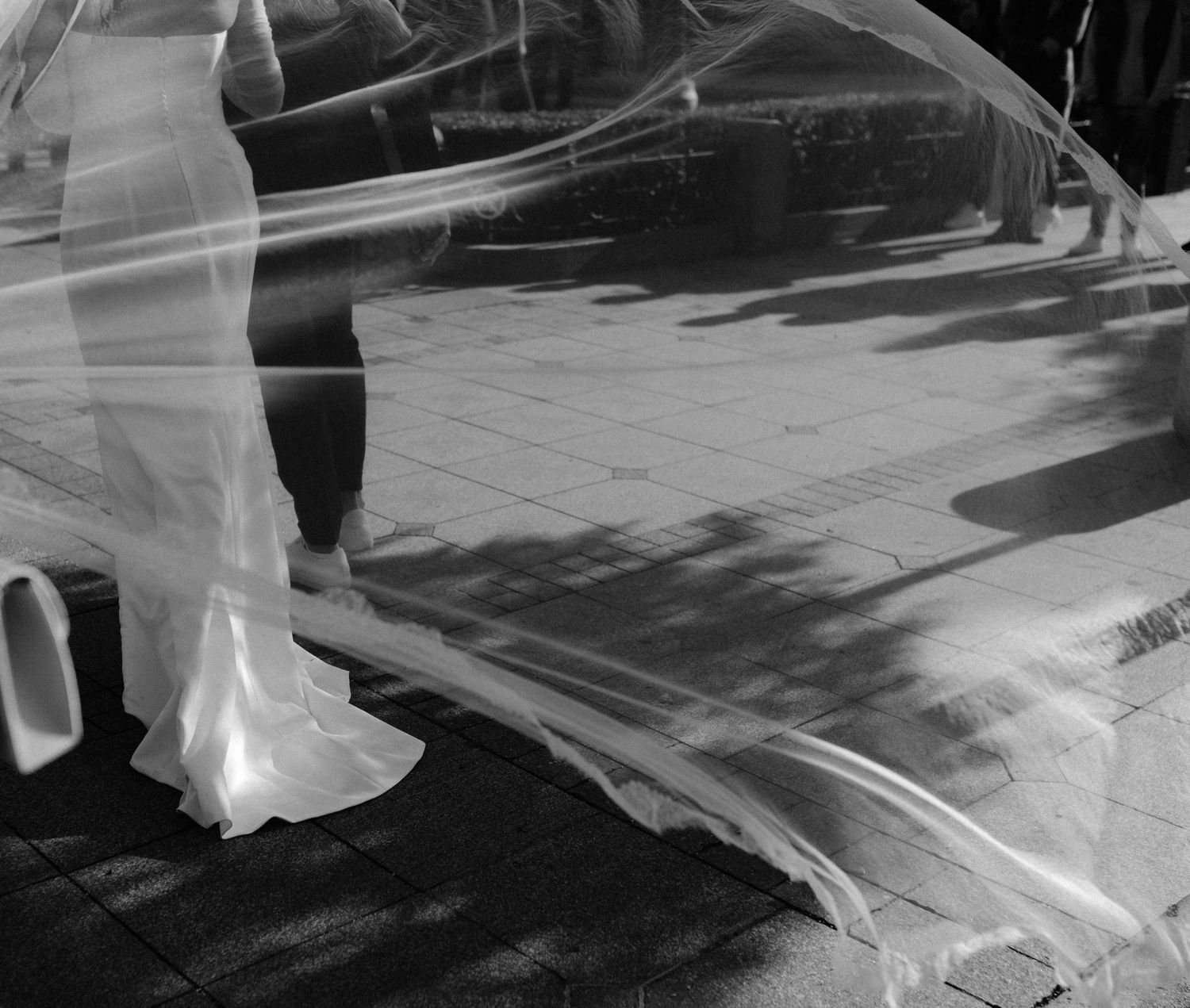 A black and white photograph showing a series of reflections in a window display with silhouettes passing by.