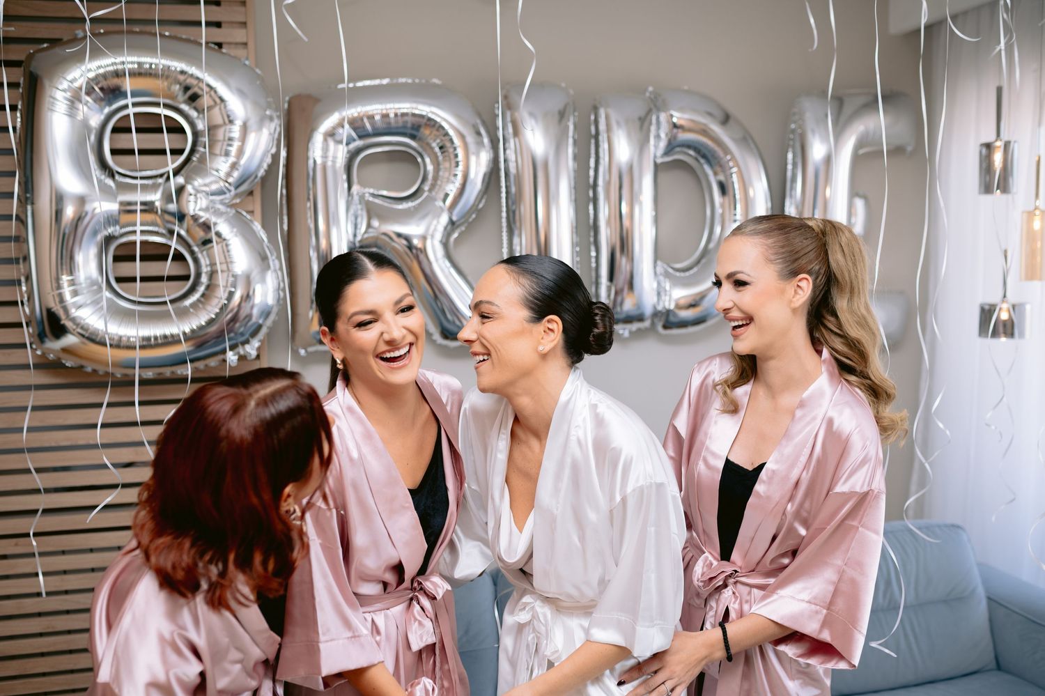 A group in matching pink and white robes celebrates with silver balloons and champagne at a special event.