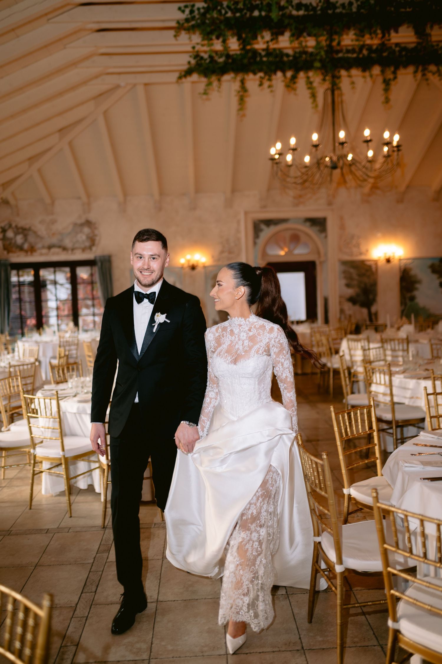 Elegant wedding reception venue with white chairs, chandeliers, and floral decor creating a romantic atmosphere.