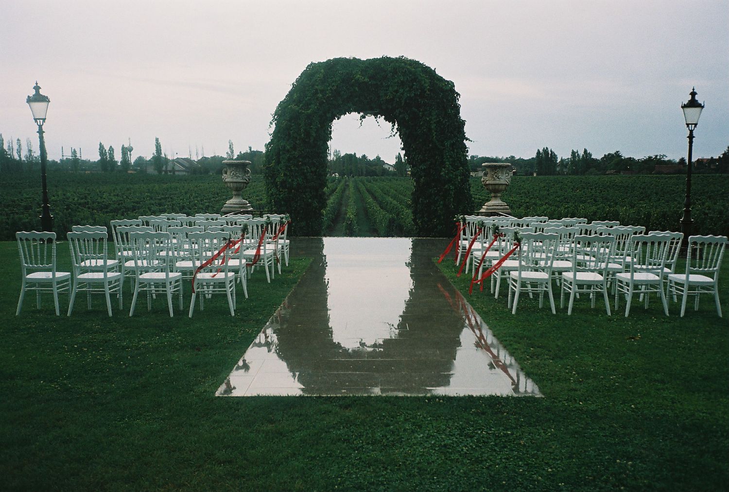 White chairs set up for an outdoor wedding ceremony on a lush green lawn with a white aisle runner.