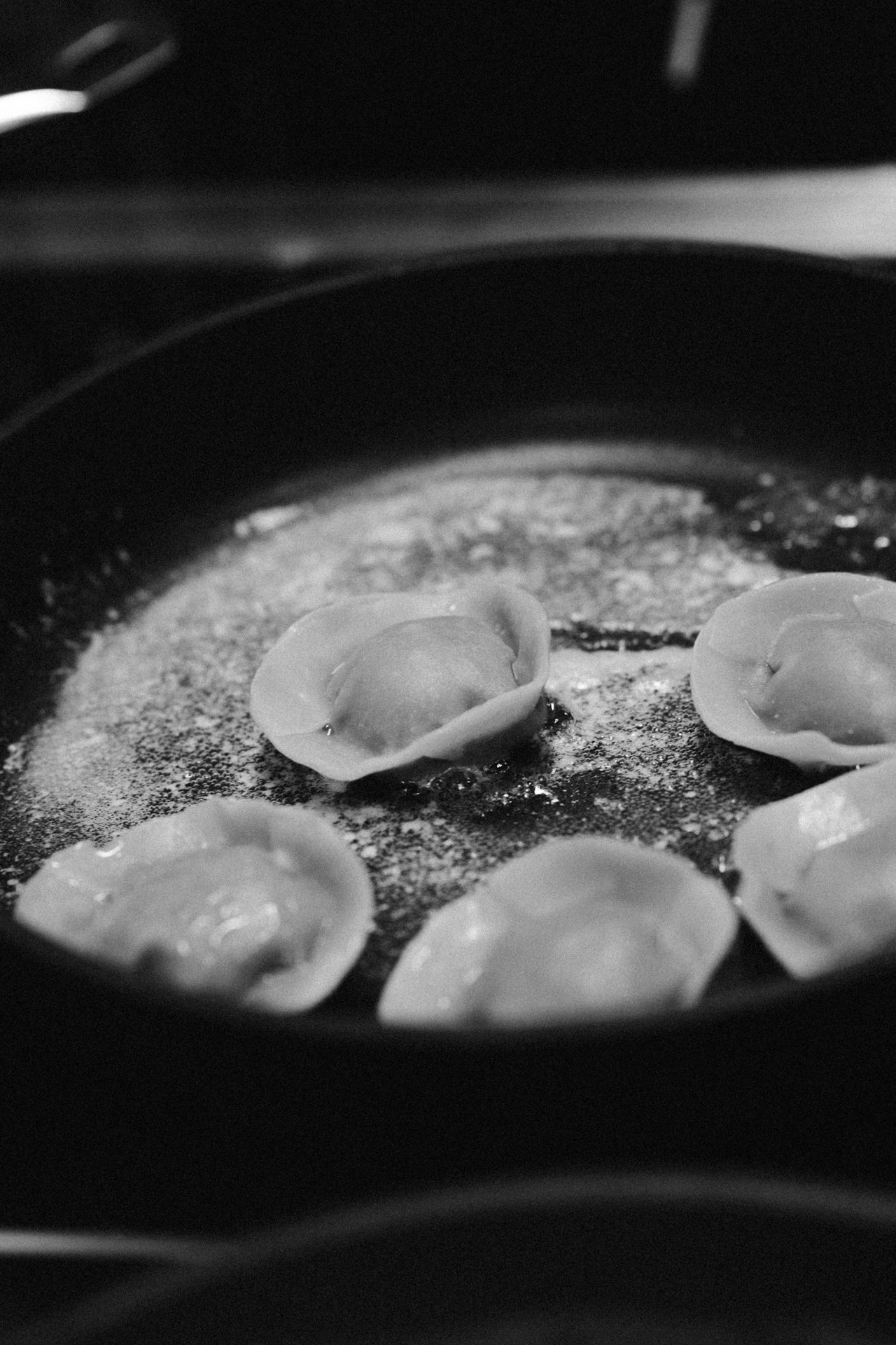 Black and white close-up photo of dumplings cooking in a pan with flour dusting.