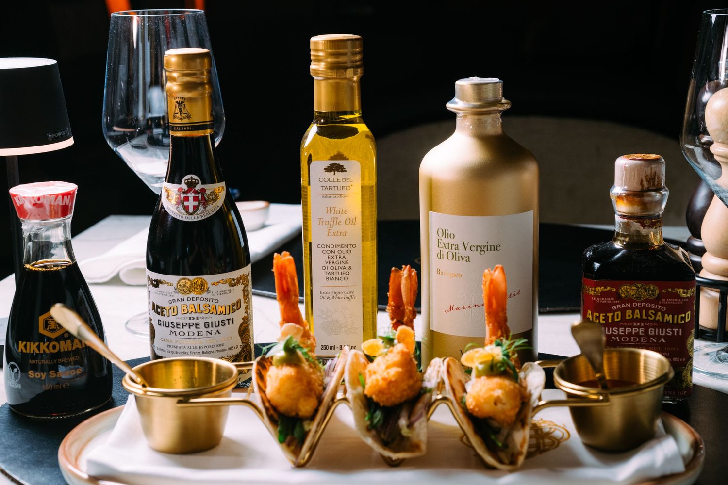 A collection of golden liquor bottles and cocktail mixing equipment arranged on a dark wooden surface.