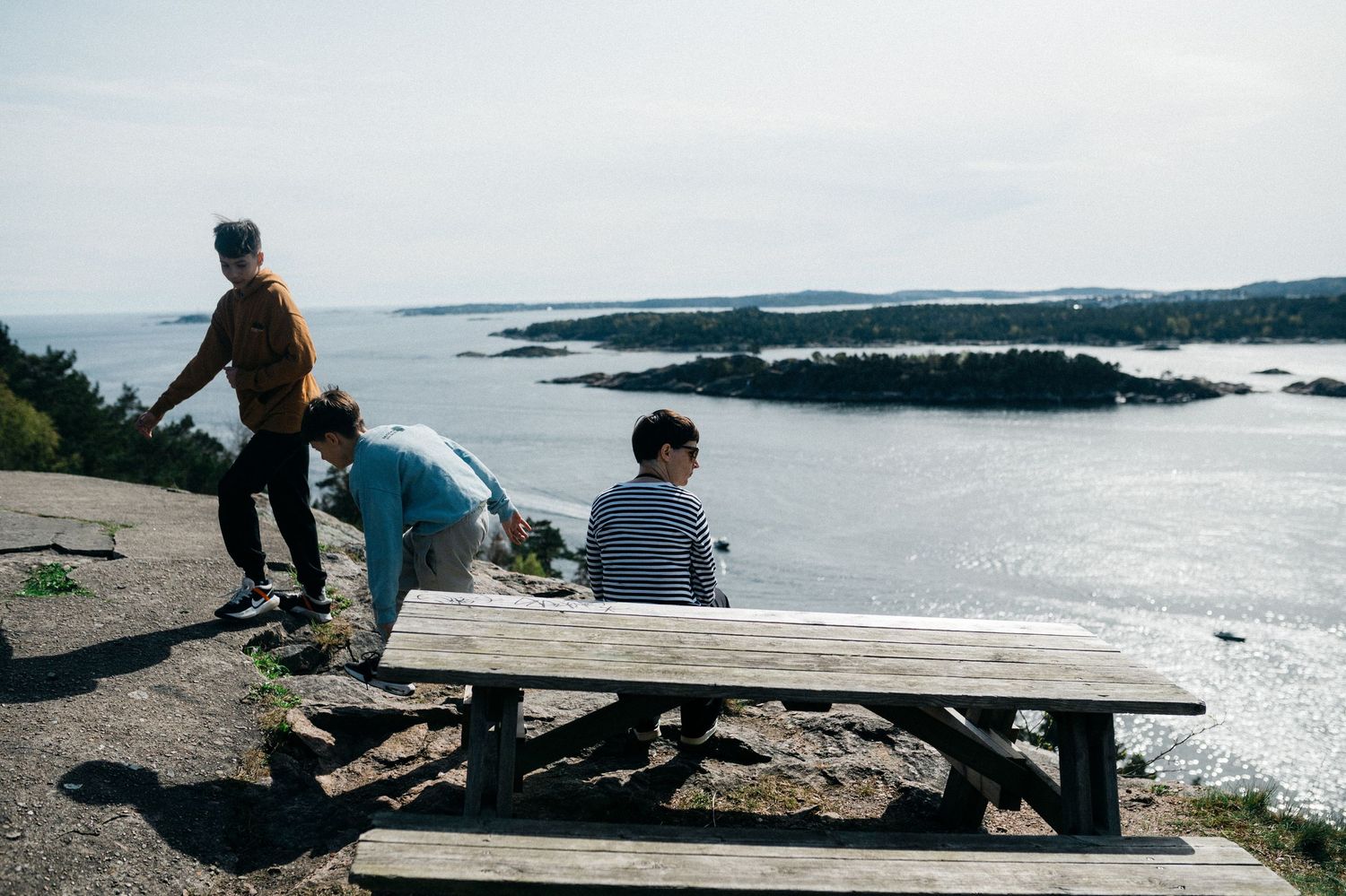 A group sits together at a wooden picnic table overlooking a scenic coastal landscape on a cloudy day.