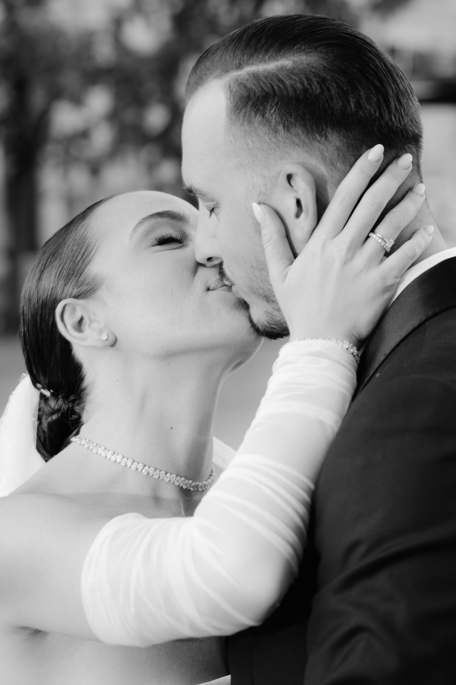 A bride and groom hold hands in front of a grand church building during a sunlit black and white wedding photoshoot.
