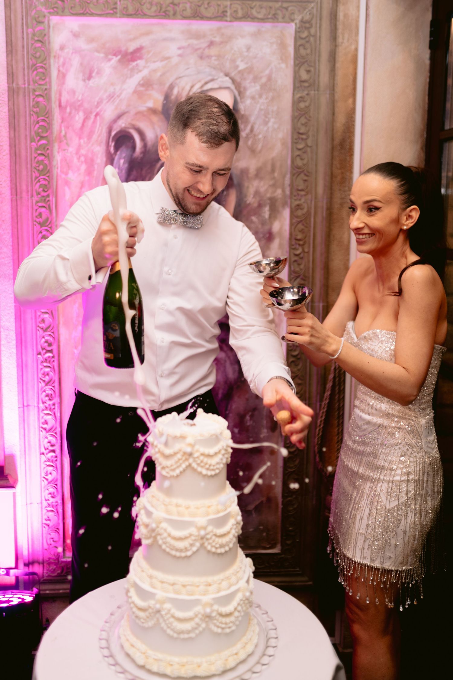 A sequence of wedding photos shows a couple cutting their elegant white tiered cake with pink lighting in the background.