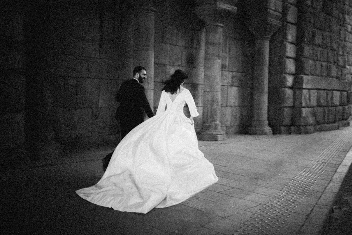 Dramatična crno-bijela fotografija vjenčanice koja leprša uz arhitekturu od kamenog zida u Beogradu.