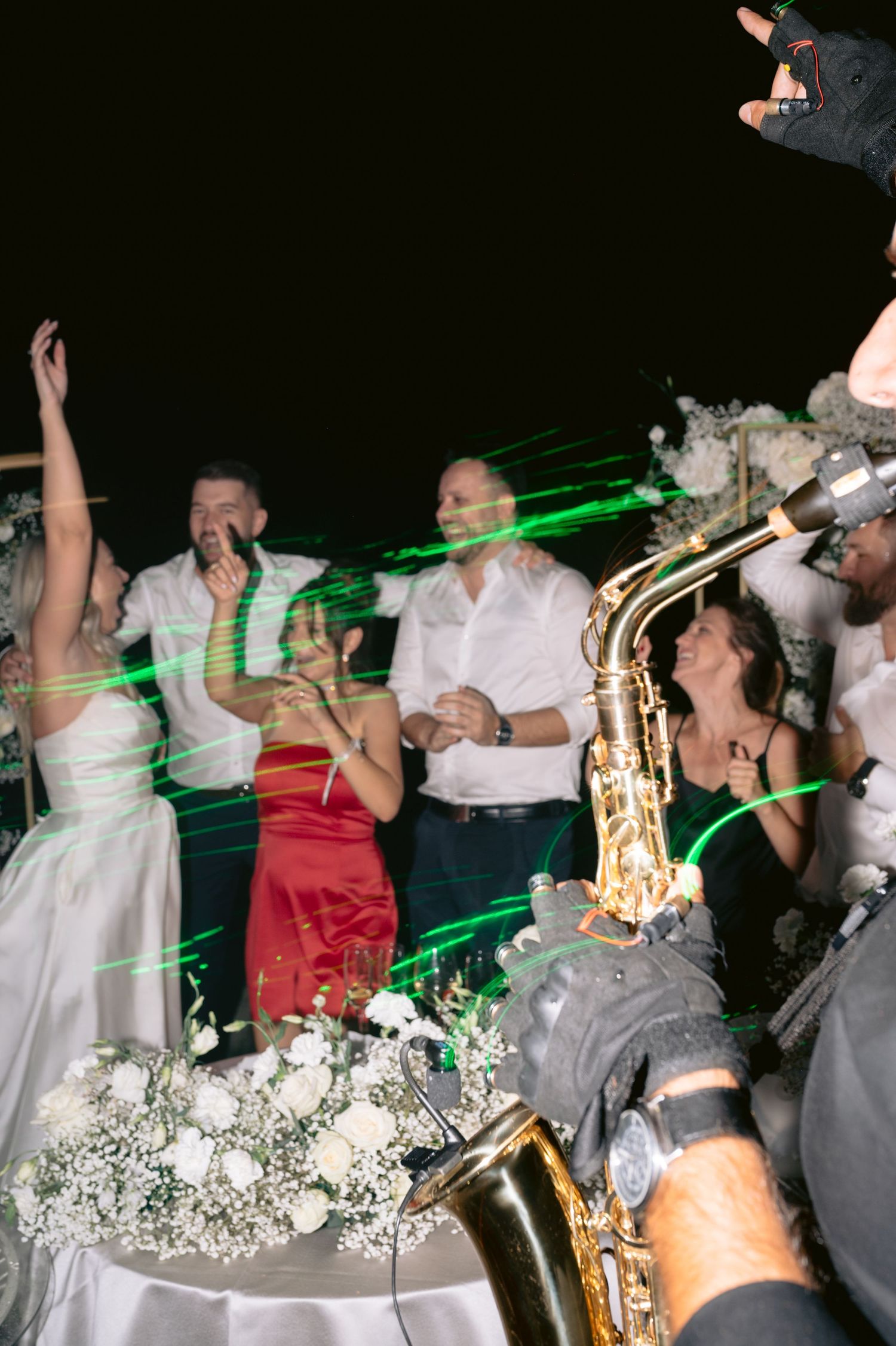 Wedding reception celebration with bride, guests, saxophone player, and green laser lights at night.
