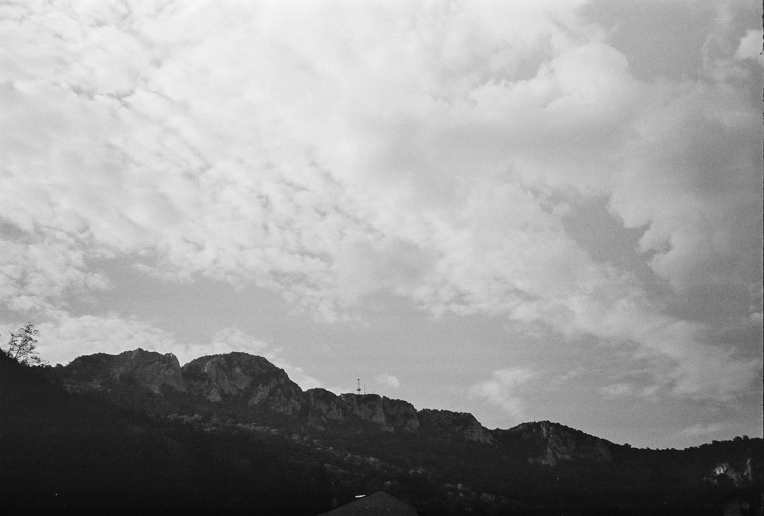 A dramatic black and white landscape photograph showing mountain silhouettes against a cloudy sky.