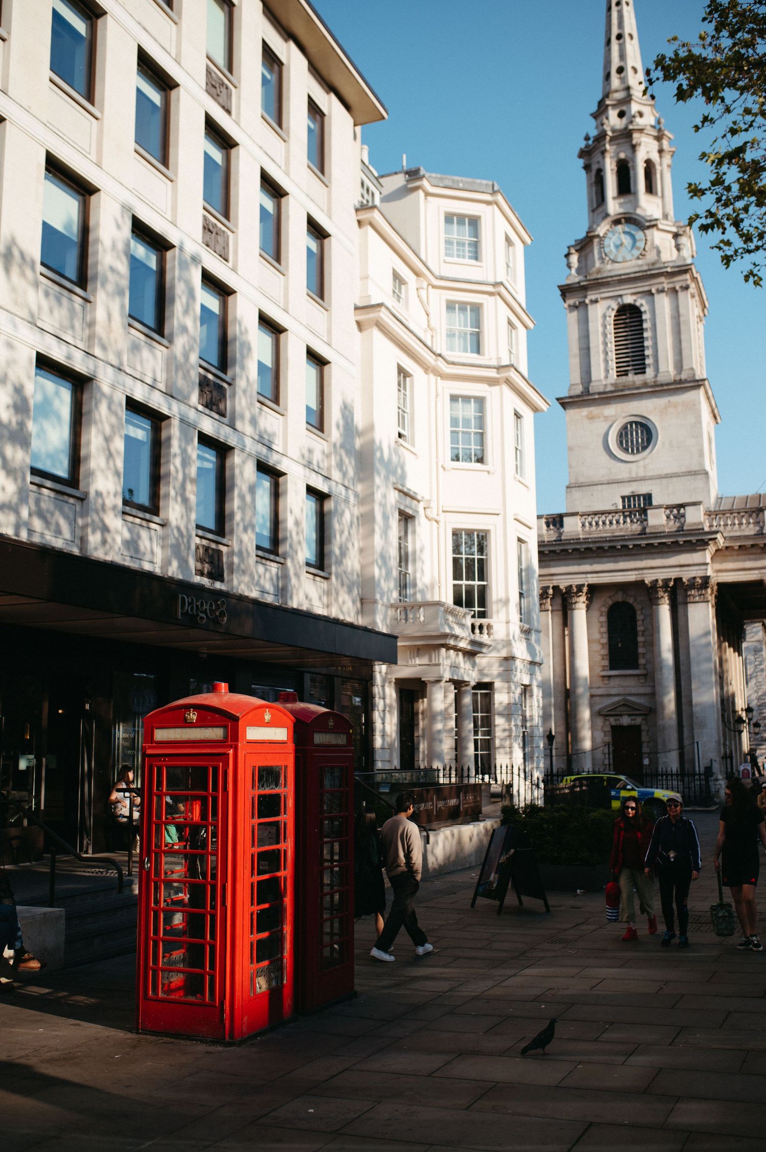 Classic red British telephone boxes stand against white Georgian architecture and church spires in London's historic streets.