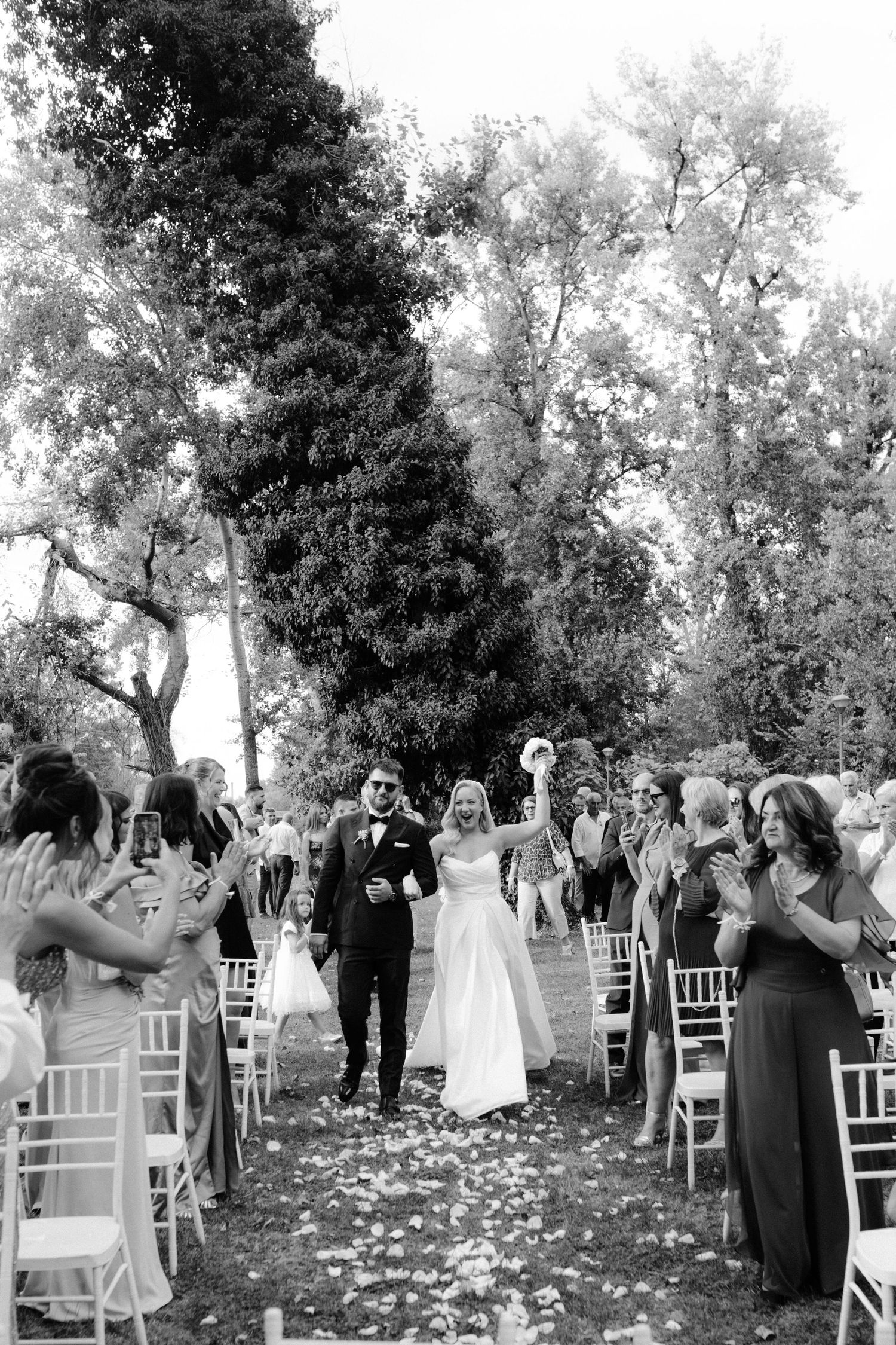Black and white photo of a joyful bride and groom walking down the aisle after their outdoor wedding ceremony.