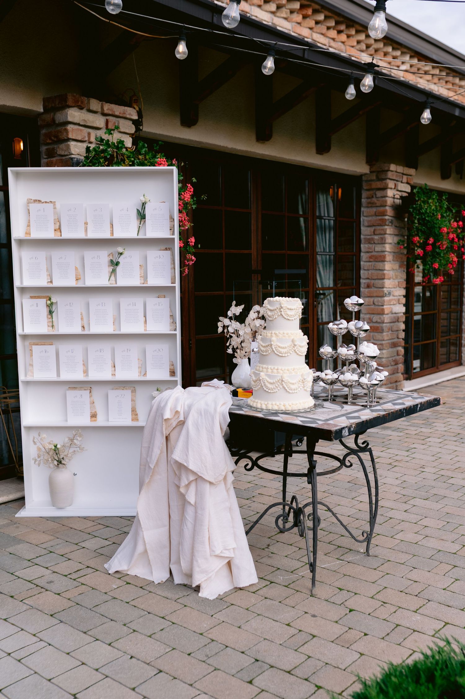 Wedding reception display with white cake, gift table, and elegant seating arrangements on a stone patio.