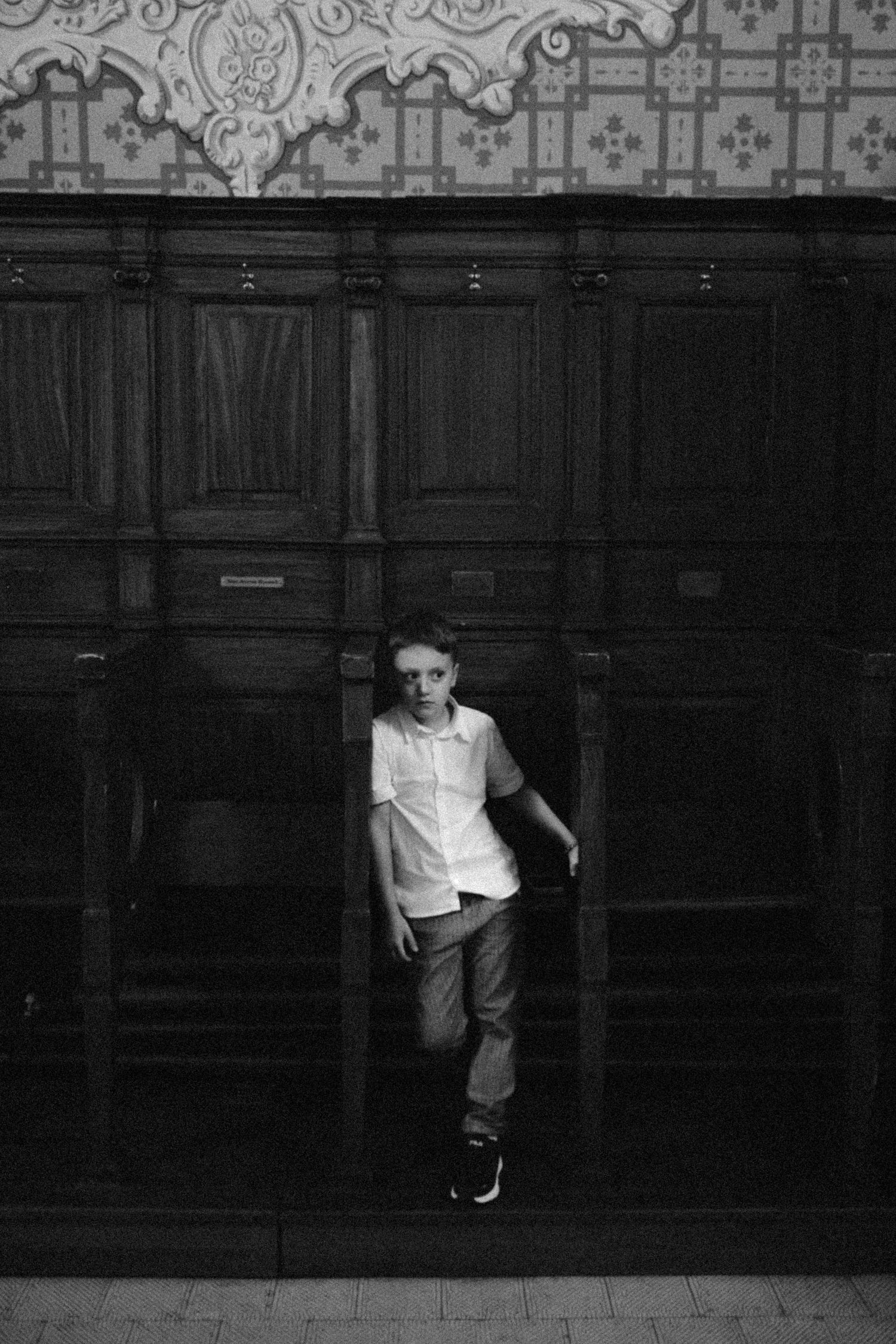 A black and white sequence of images showing a figure moving along a dark wall in a dramatic dance-like motion.