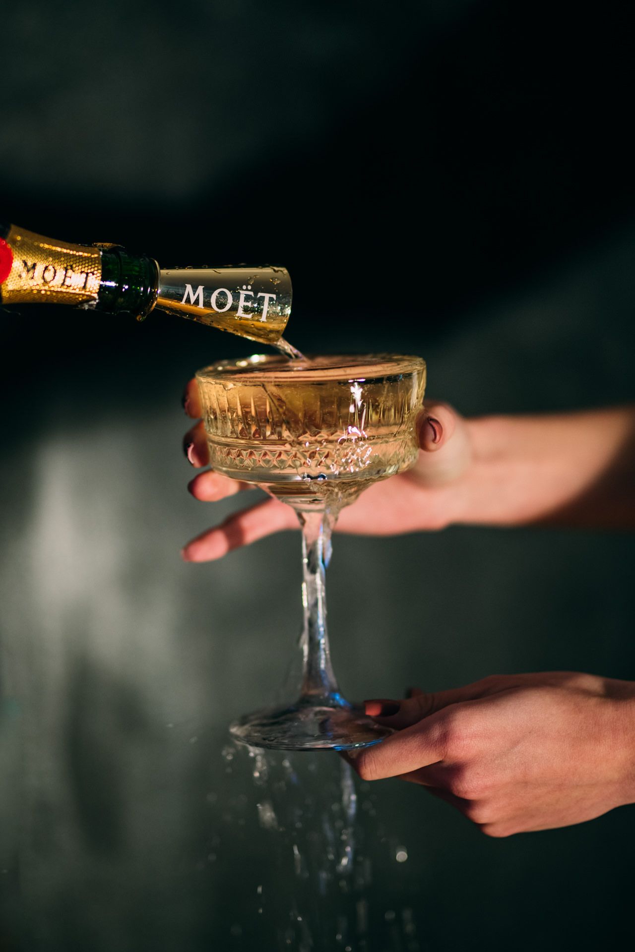 Champagne being poured into vintage Moet coupe glasses in dramatic lighting.